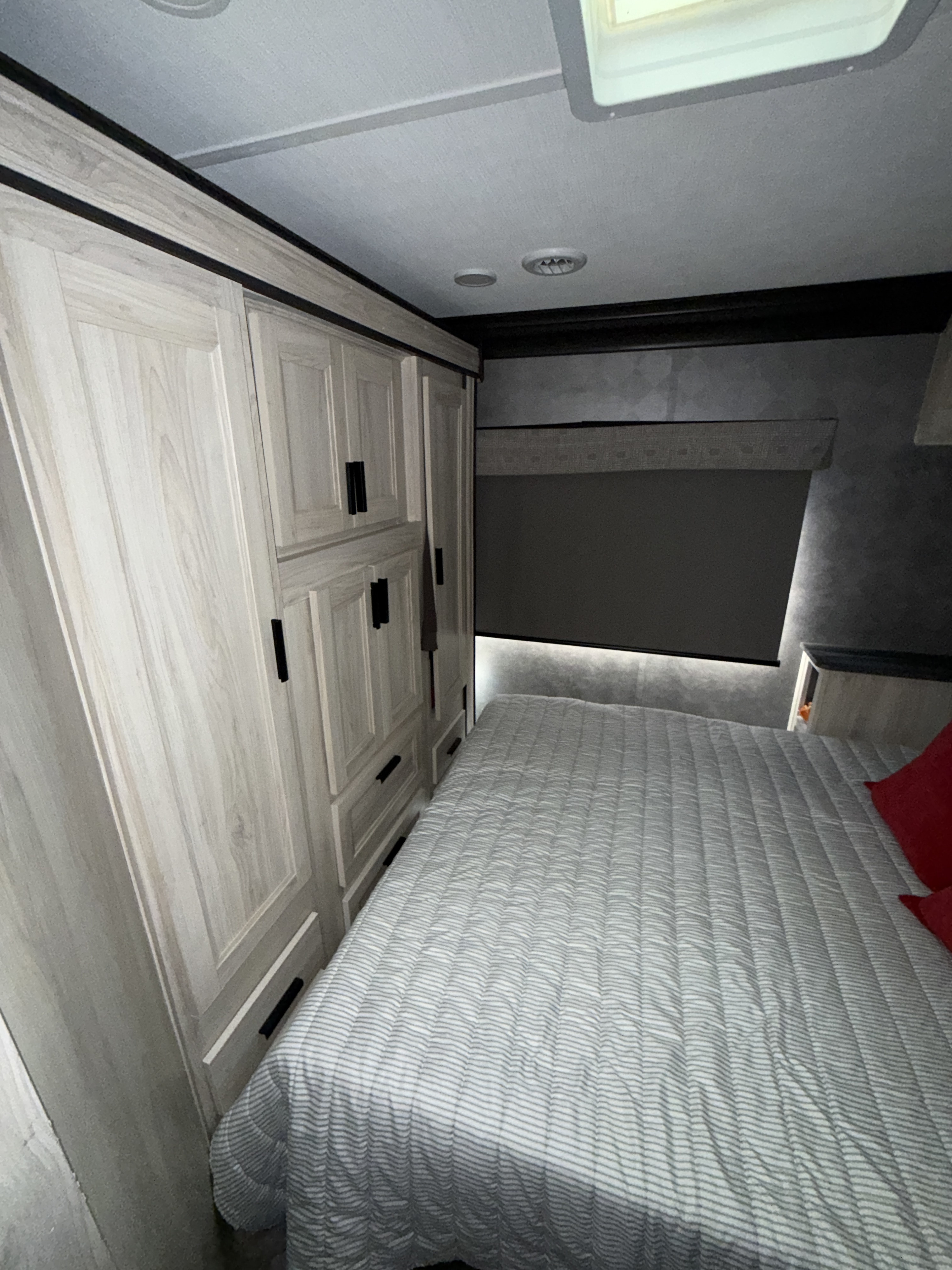 Compact RV rental bedroom featuring light wood storage, a cozy bed with striped comforter, and a pulled-down window shade.. Forest River Sunseeker LE 2023