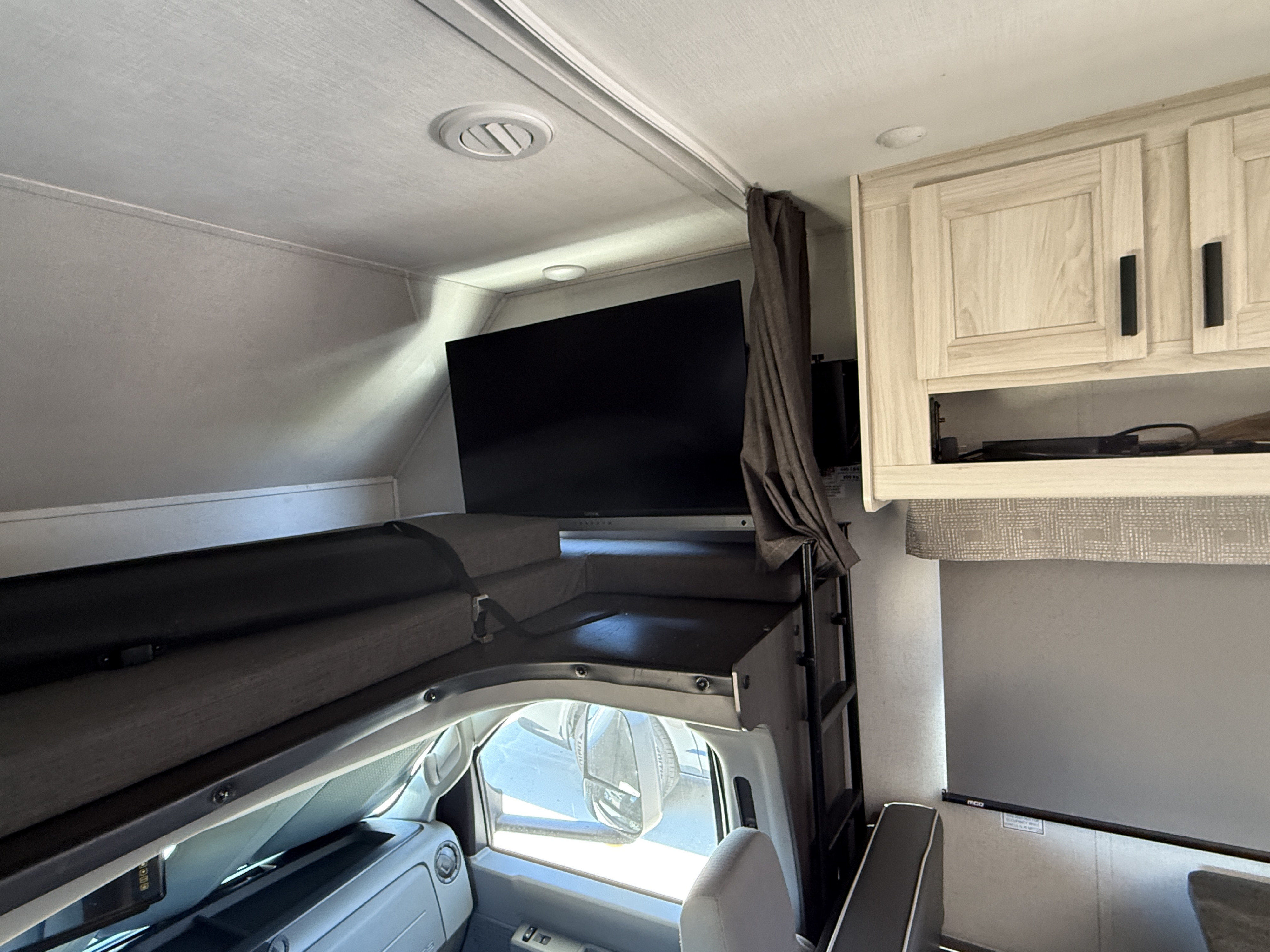 Cozy RV rental interior with an overhead bunk bed, mounted TV, light wood cabinets, and driver's cab view.. Forest River Sunseeker LE 2023