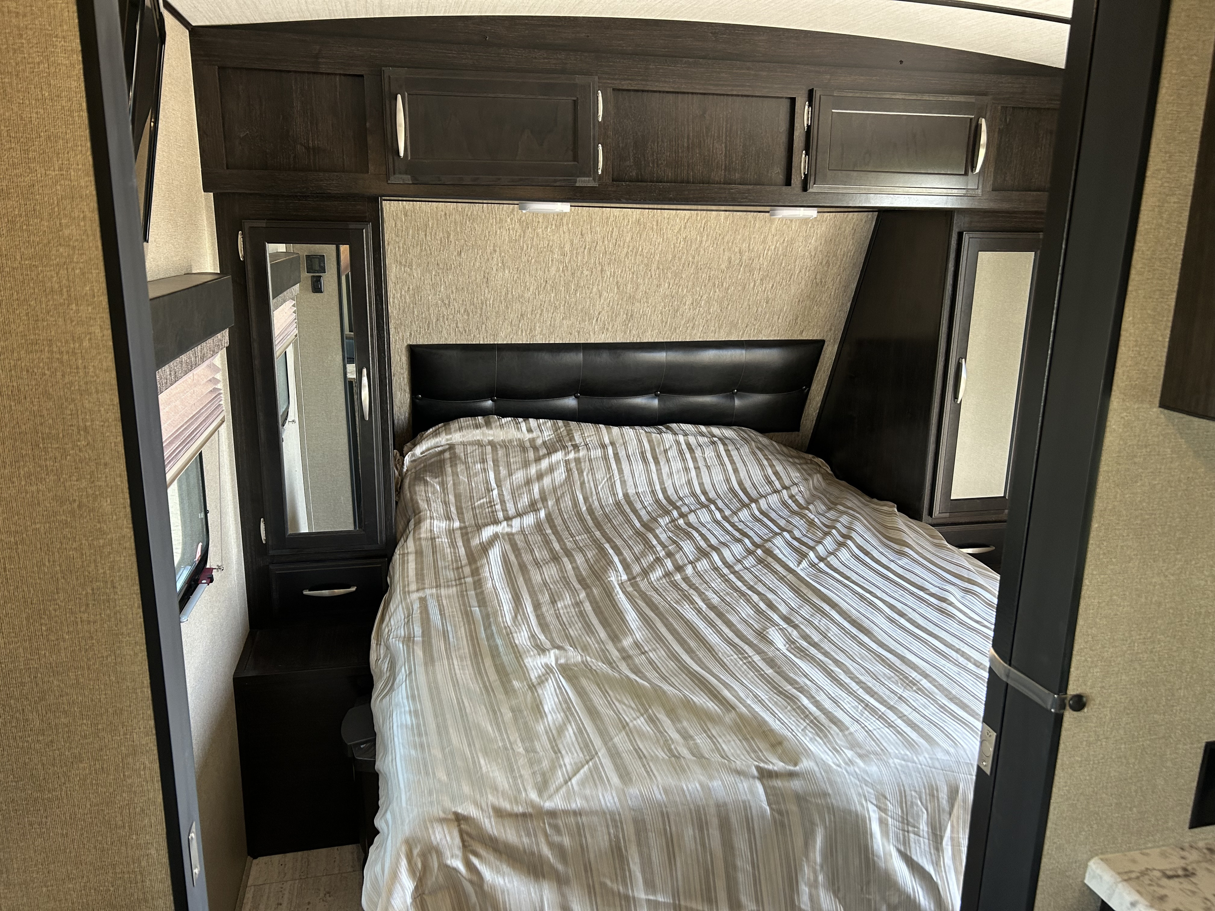 RV rental bedroom with a comfortable queen bed, striped duvet, dark wood cabinets, and mirrored wardrobes, offering cozy accommodation.. Grand Design Imagine 2018