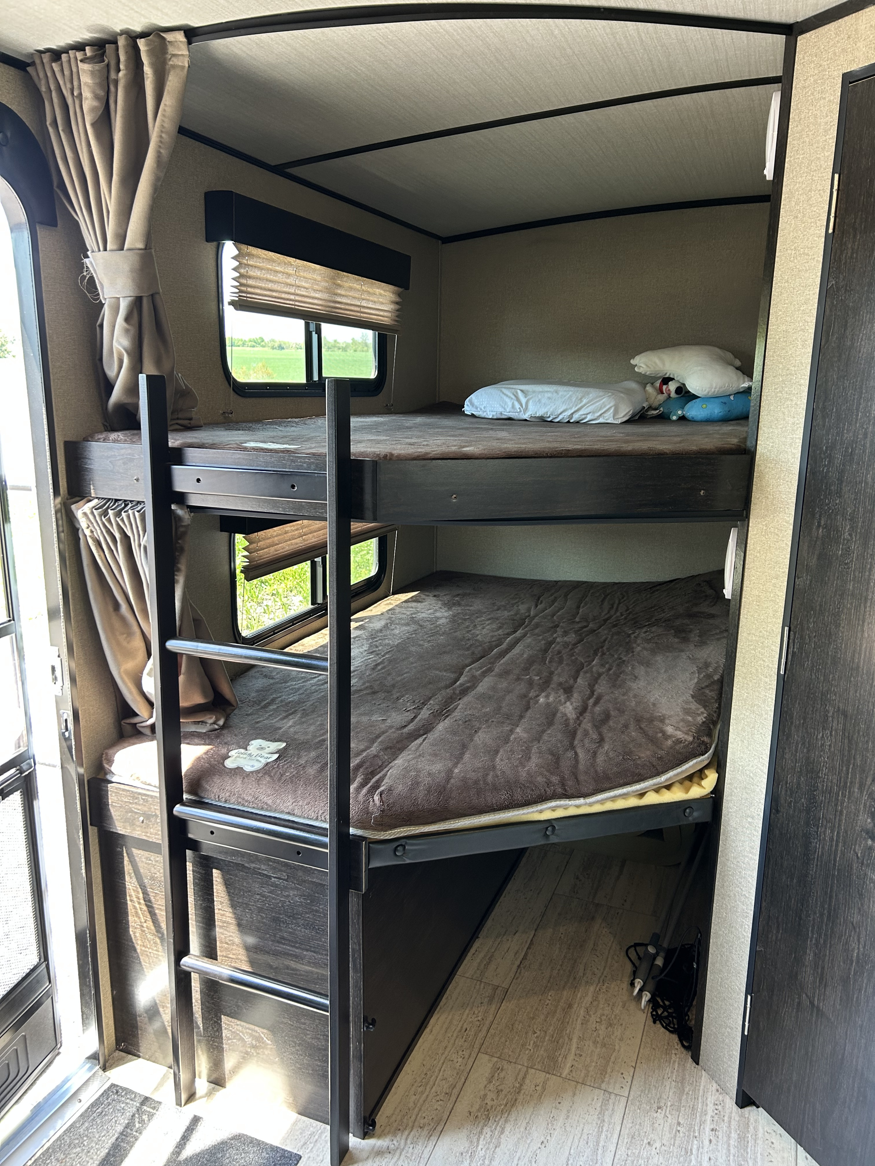RV rental interior features comfortable bunk beds with soft blankets, windows showing green fields, and curtains. Perfect for family adventures.. Grand Design Imagine 2018