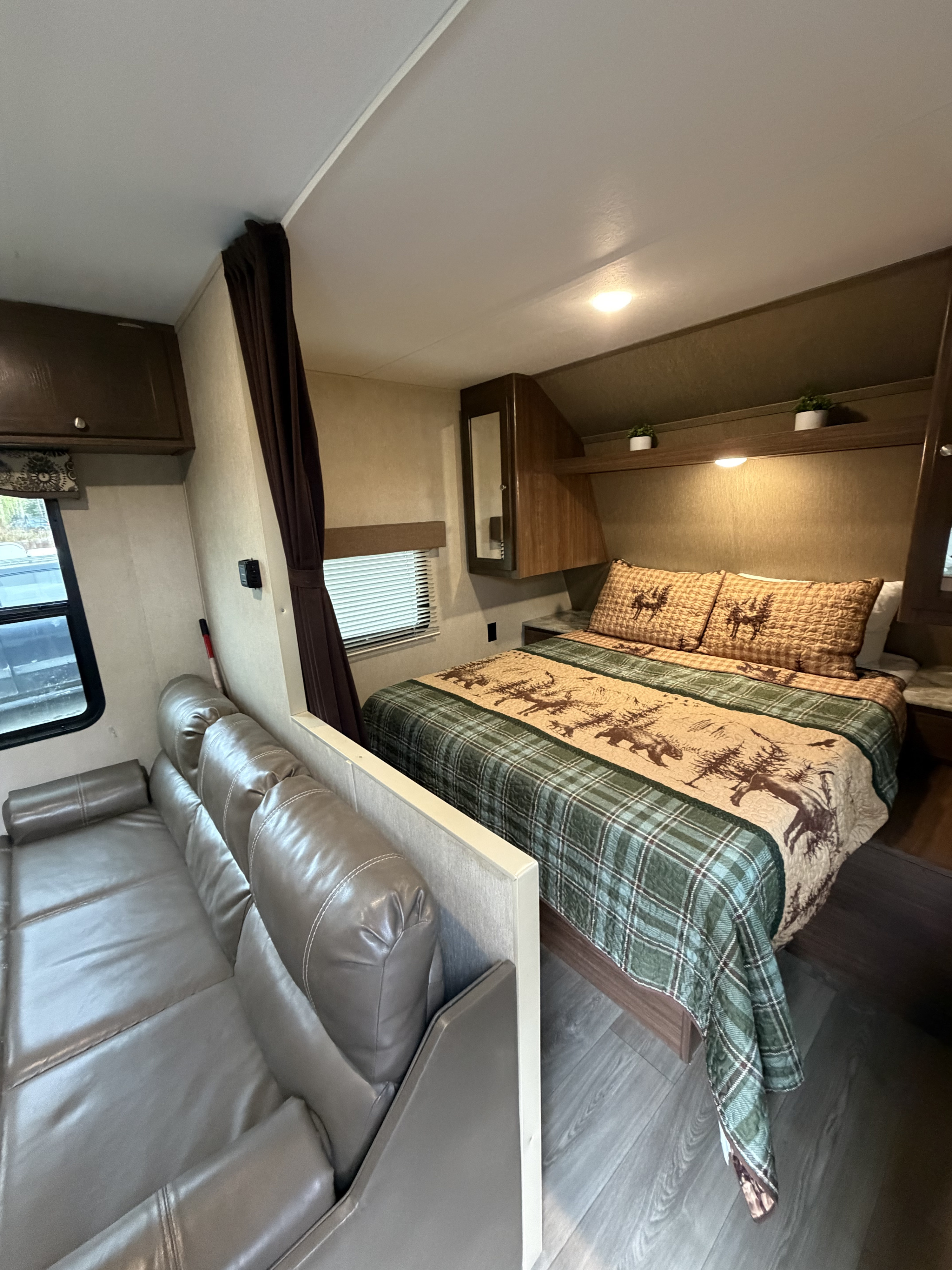 Experience comfort in this RV rental featuring a rustic bedroom with a plaid quilt and a plush gray sofa in the living area.. Dutchmen Coleman Lantern 2018