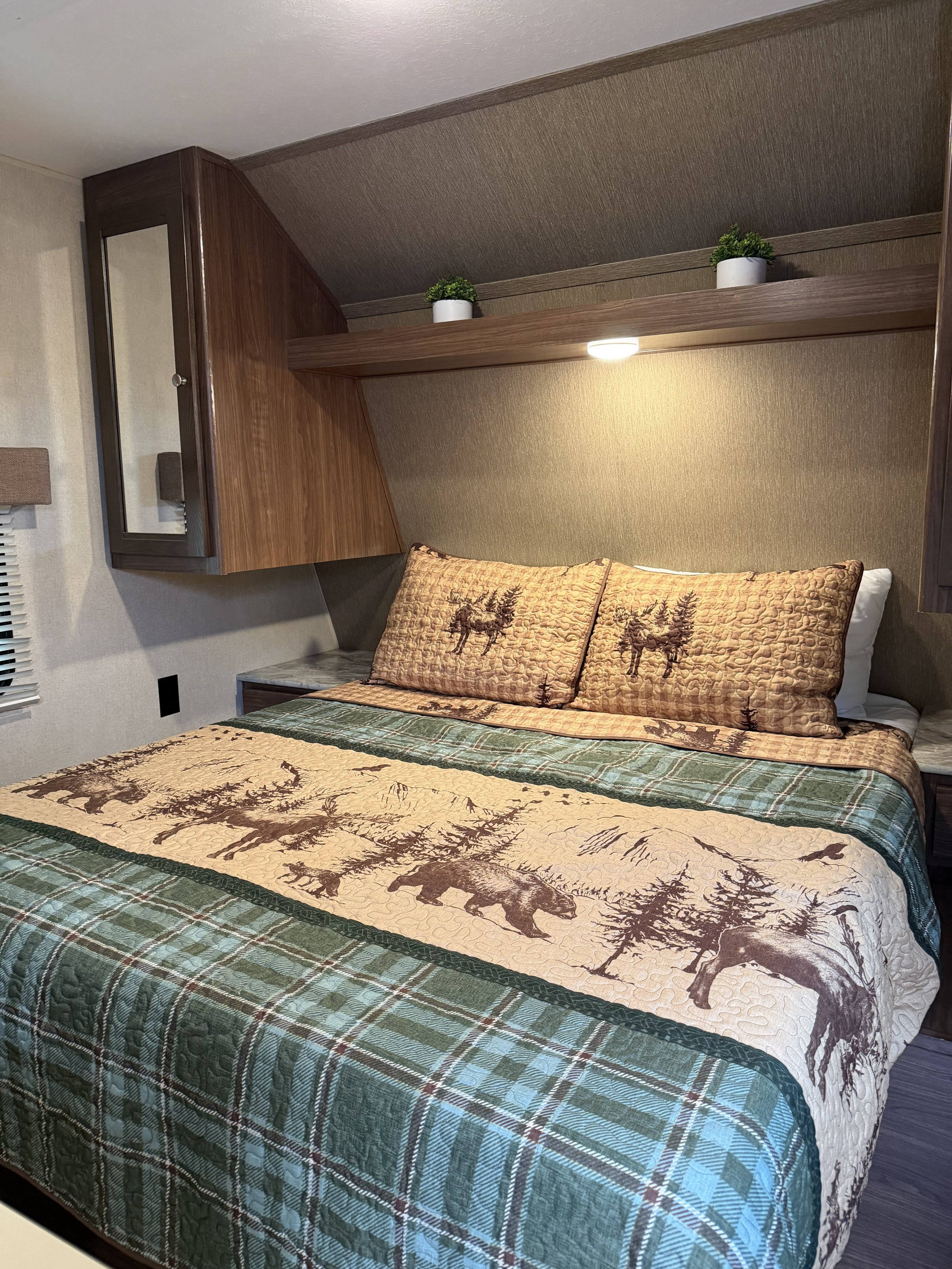Cozy RV rental bedroom featuring nature-themed bedding with bears, deer, and a plaid quilt, perfect for a comfortable stay.. Dutchmen Coleman Lantern 2018