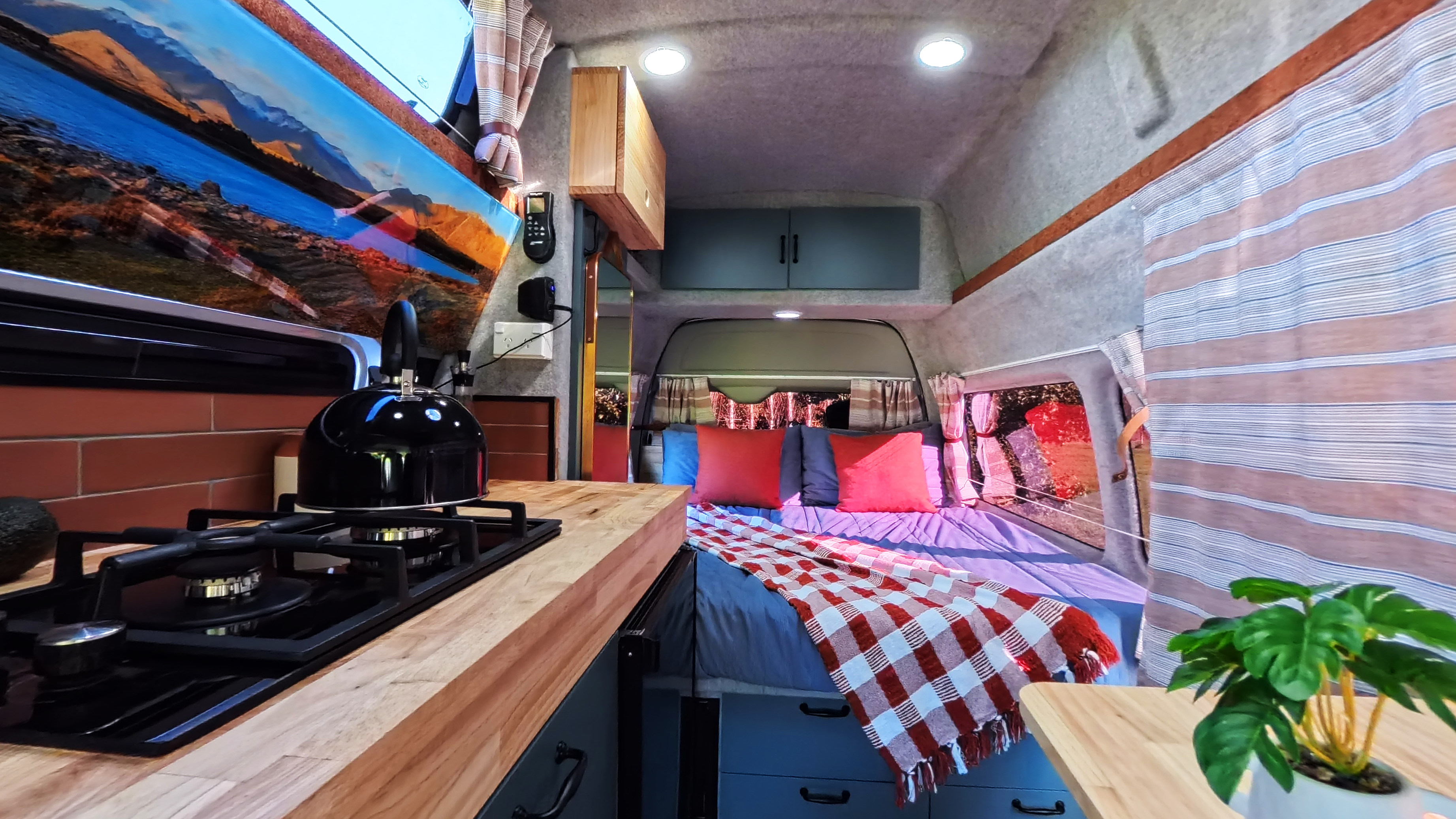 Inside this cozy RV rental, discover a kitchen with gas stove, wooden counter, and a bed with red pillows.. Other Other 2006