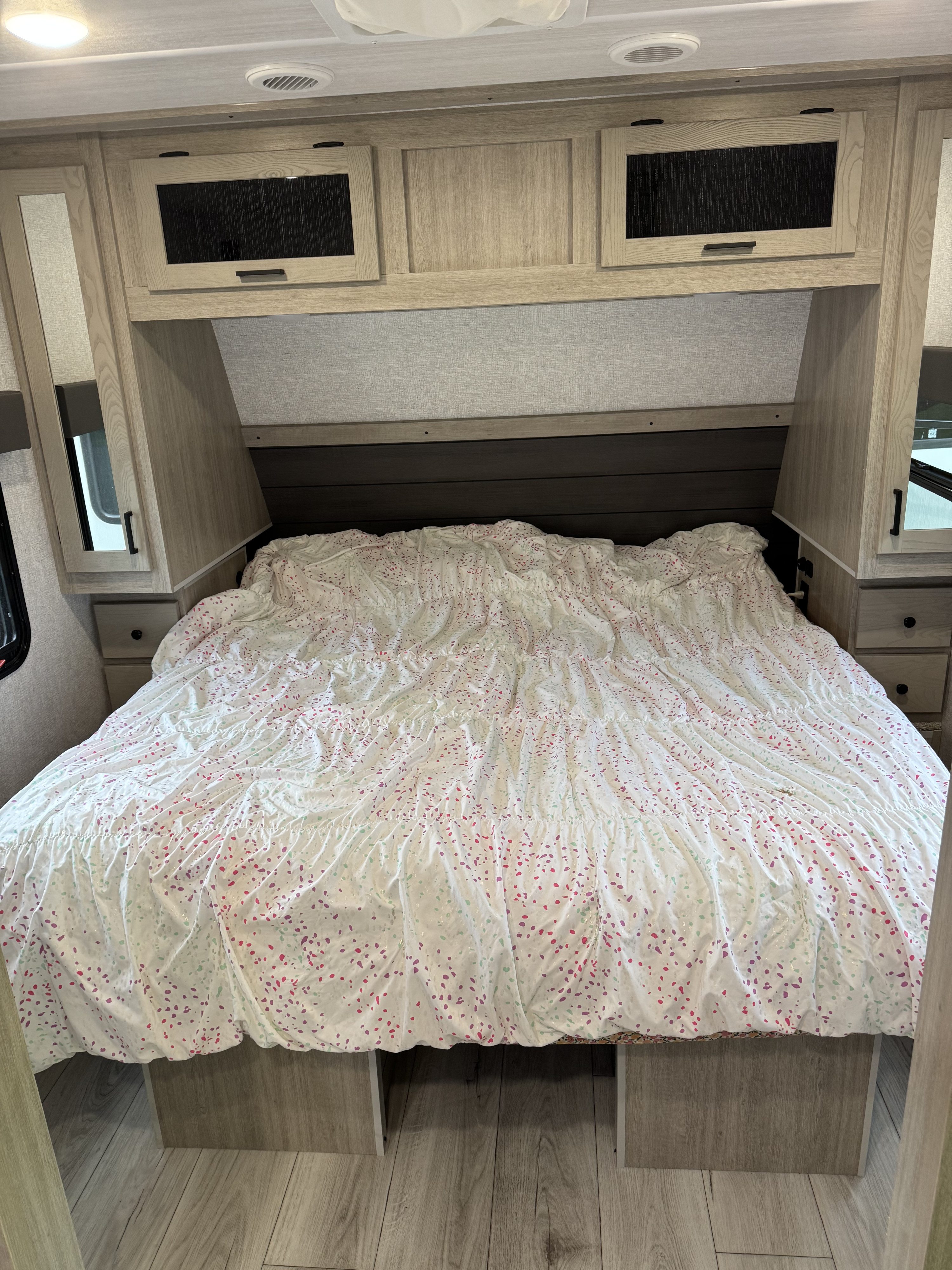 Cozy RV rental bedroom with a comfy bed, colorful duvet, overhead storage, and bedside cabinets. Ideal for travel adventures.. East to West Alta 2025
