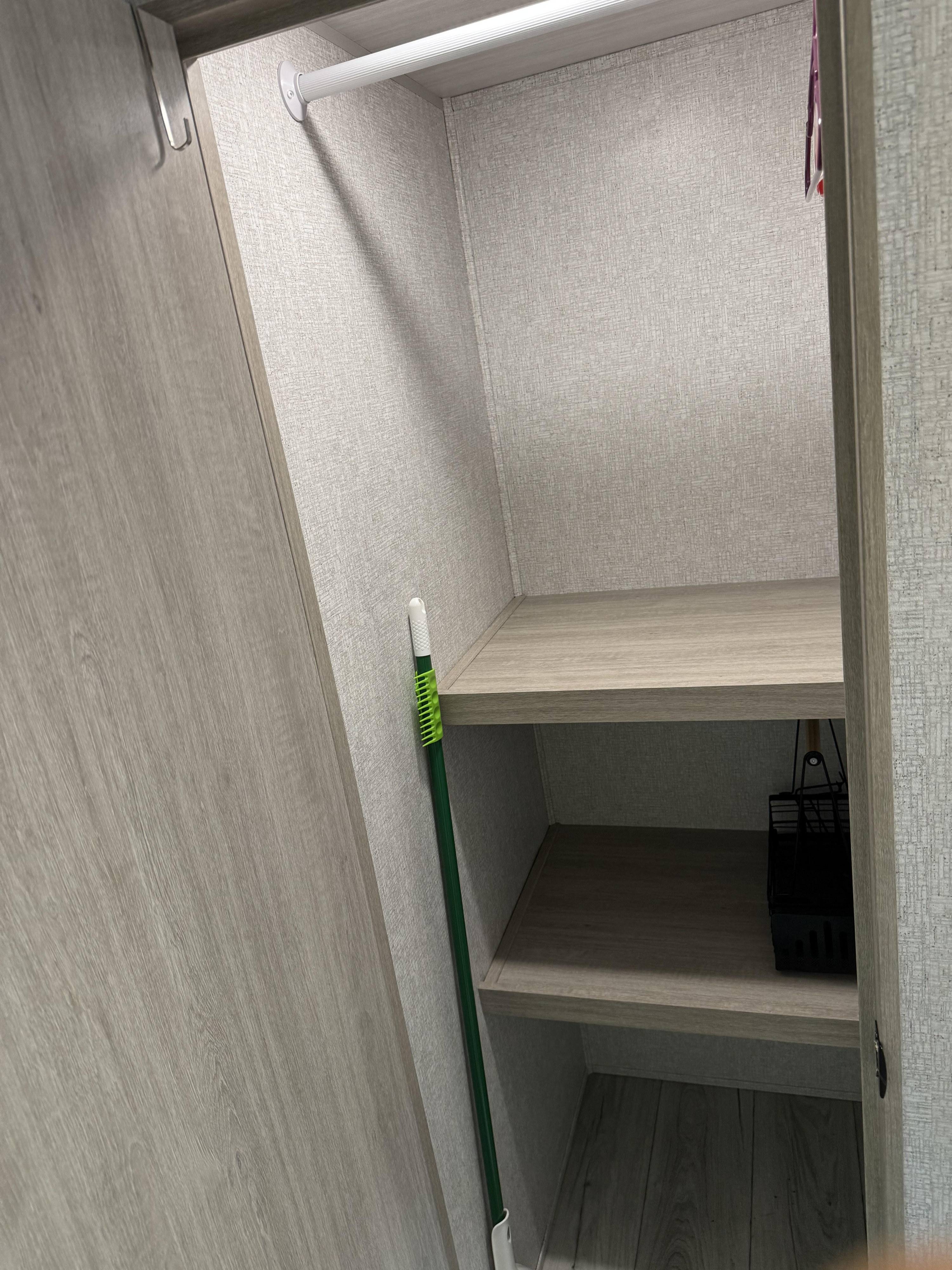 RV rental closet featuring a hanging rod, two shelves, a green broom, and a black storage basket. Efficient storage.. East to West Alta 2025
