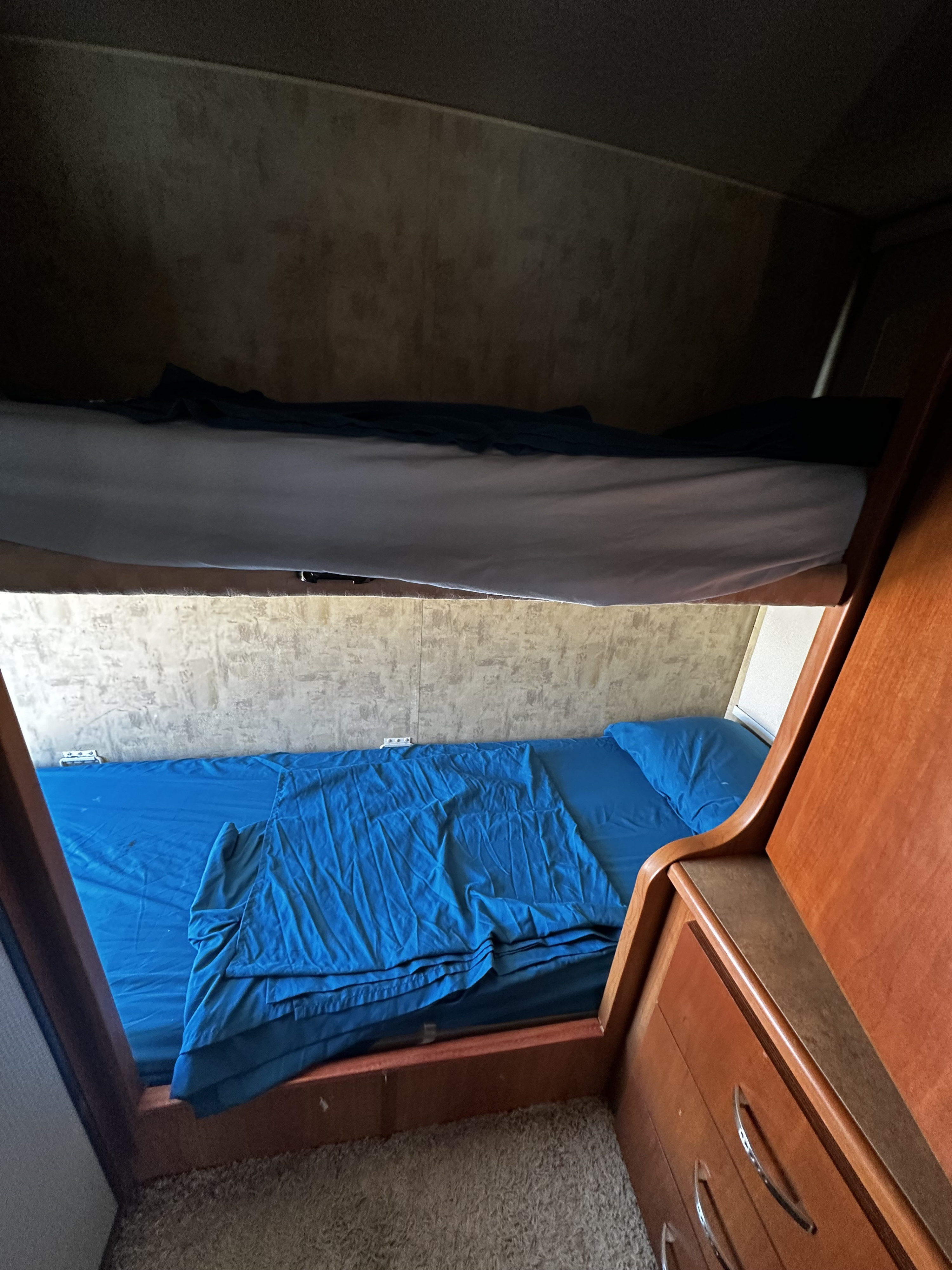 RV rental bunk beds with light and blue bedding, plus built-in wood storage, ideal for families.. Winnebago View 2006
