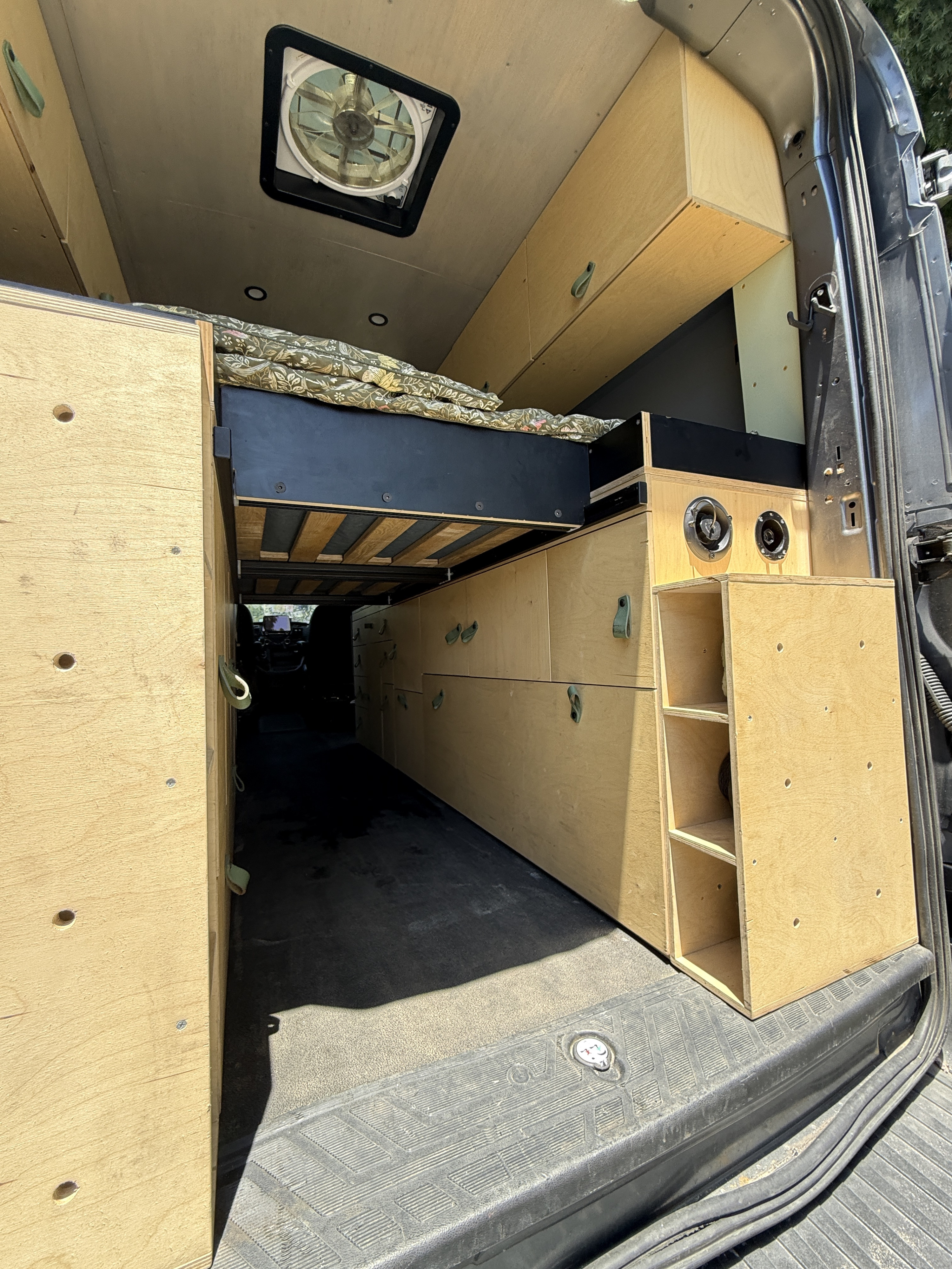 RV rental ready: custom camper van interior featuring a raised bed, plywood storage cabinets, and a ceiling fan.. Ford Transit 2021