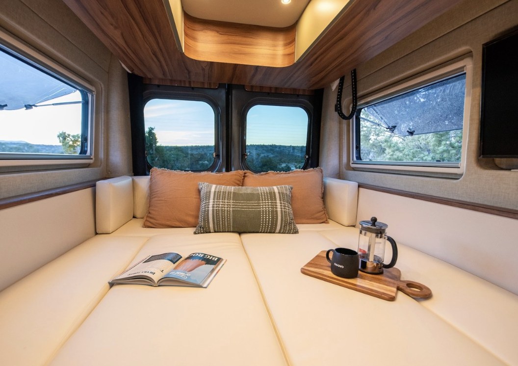 Cozy rv rental interior showing a comfortable lounge area, open book, and coffee with a scenic view outside.. Noovo Plus LB 2025
