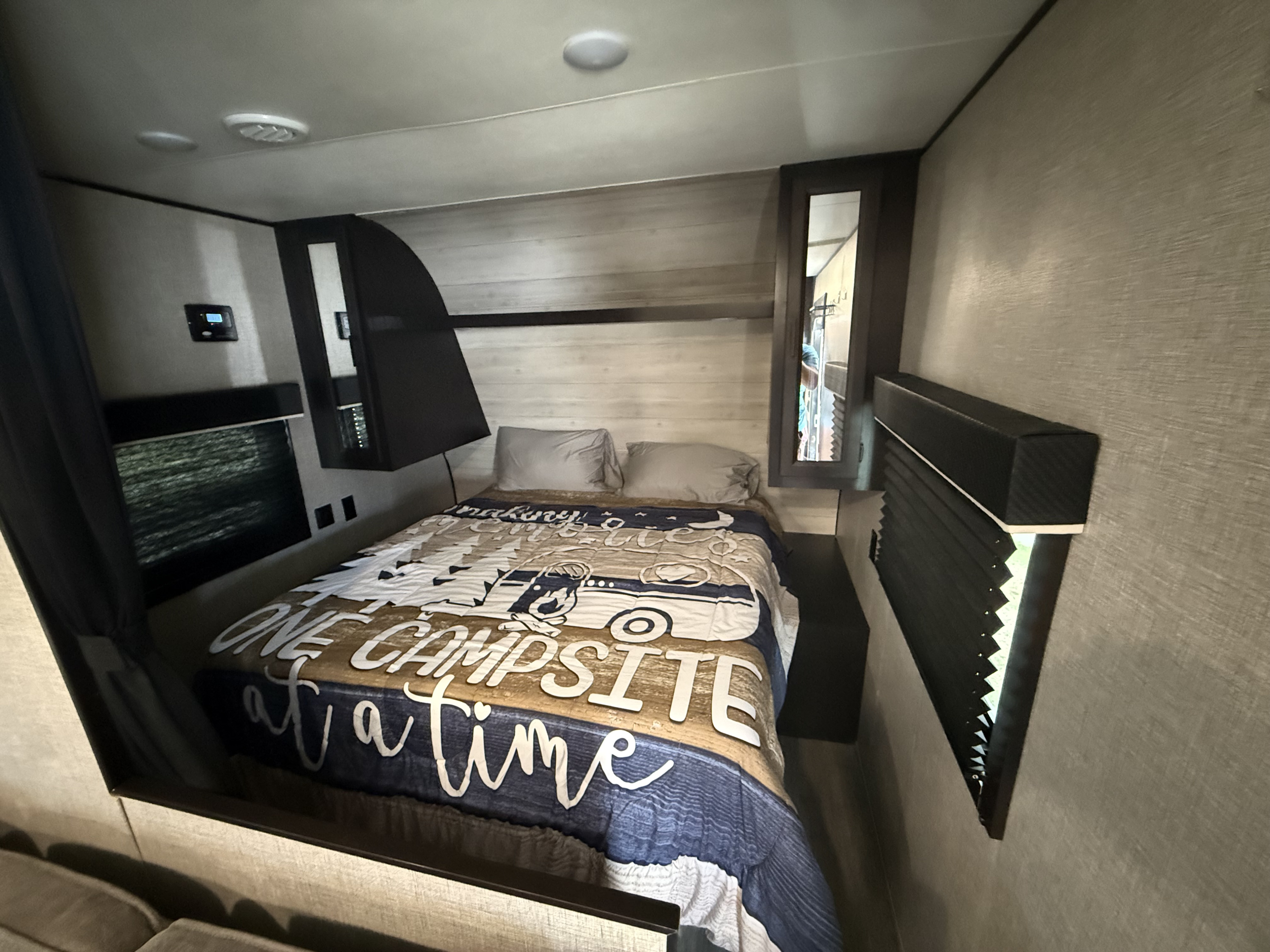 Cozy RV rental bedroom with a 'One campsite at a time' blanket, two pillows, ceiling lights, and built-in storage.. Jayco Jay Flight SLX 2022