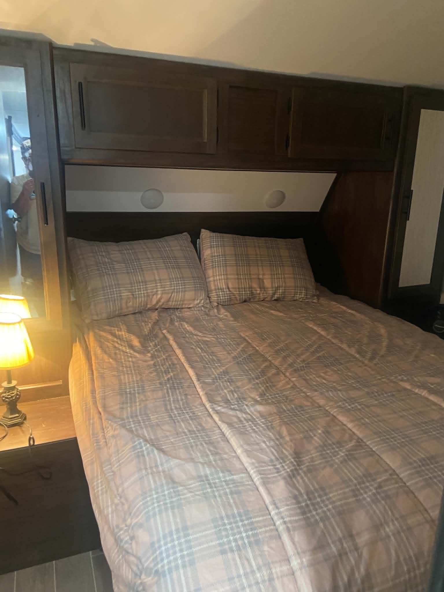 This cozy RV rental bedroom offers comfort with plaid bedding, overhead storage, and soft bedside lighting.. Forest River Cherokee Grey Wolf 2020