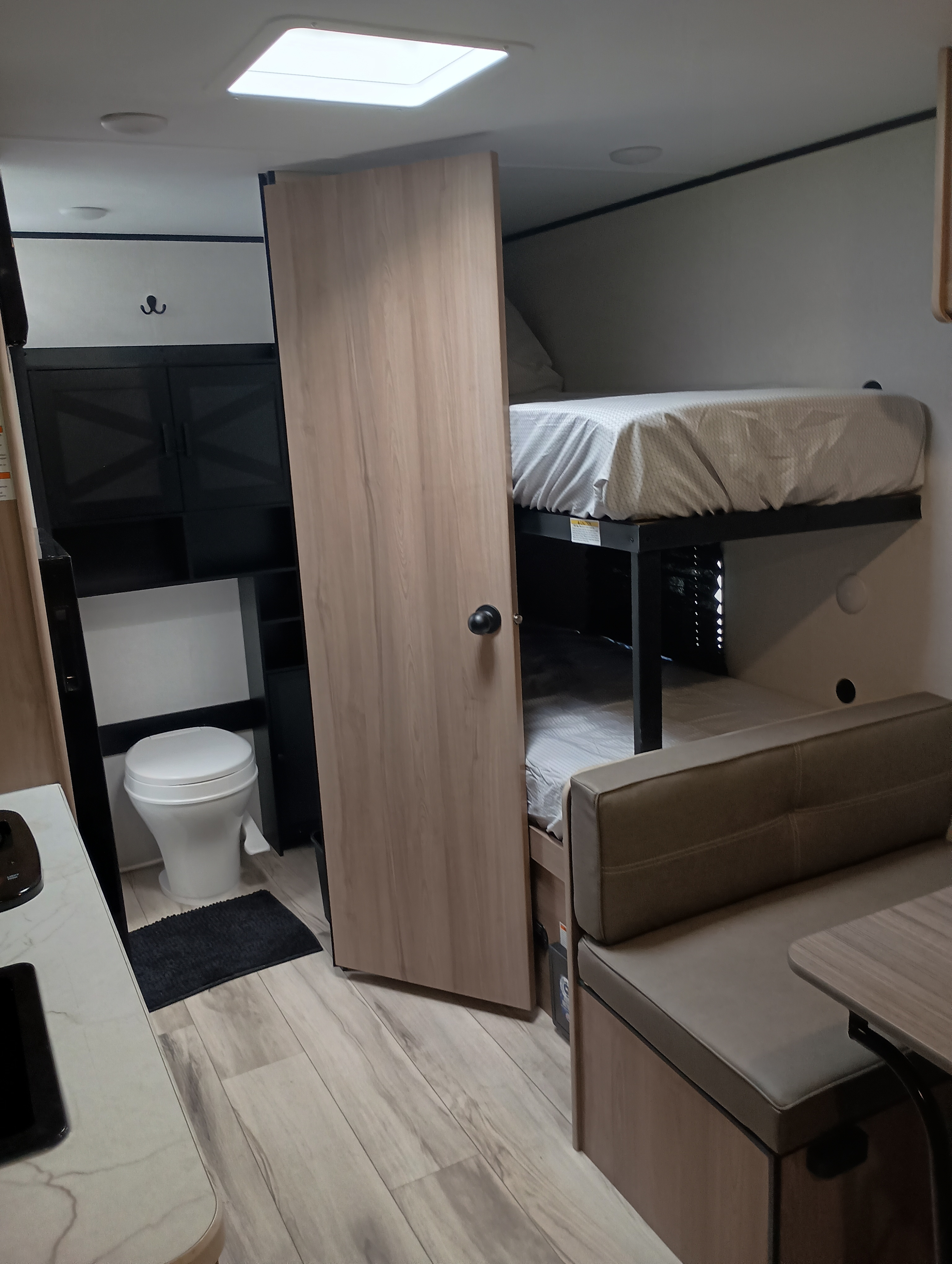 RV rental interior: A compact space with bunk beds, a toilet, and a dinette bench, featuring wood-look floors and light walls.. Dutchmen Coleman 2025