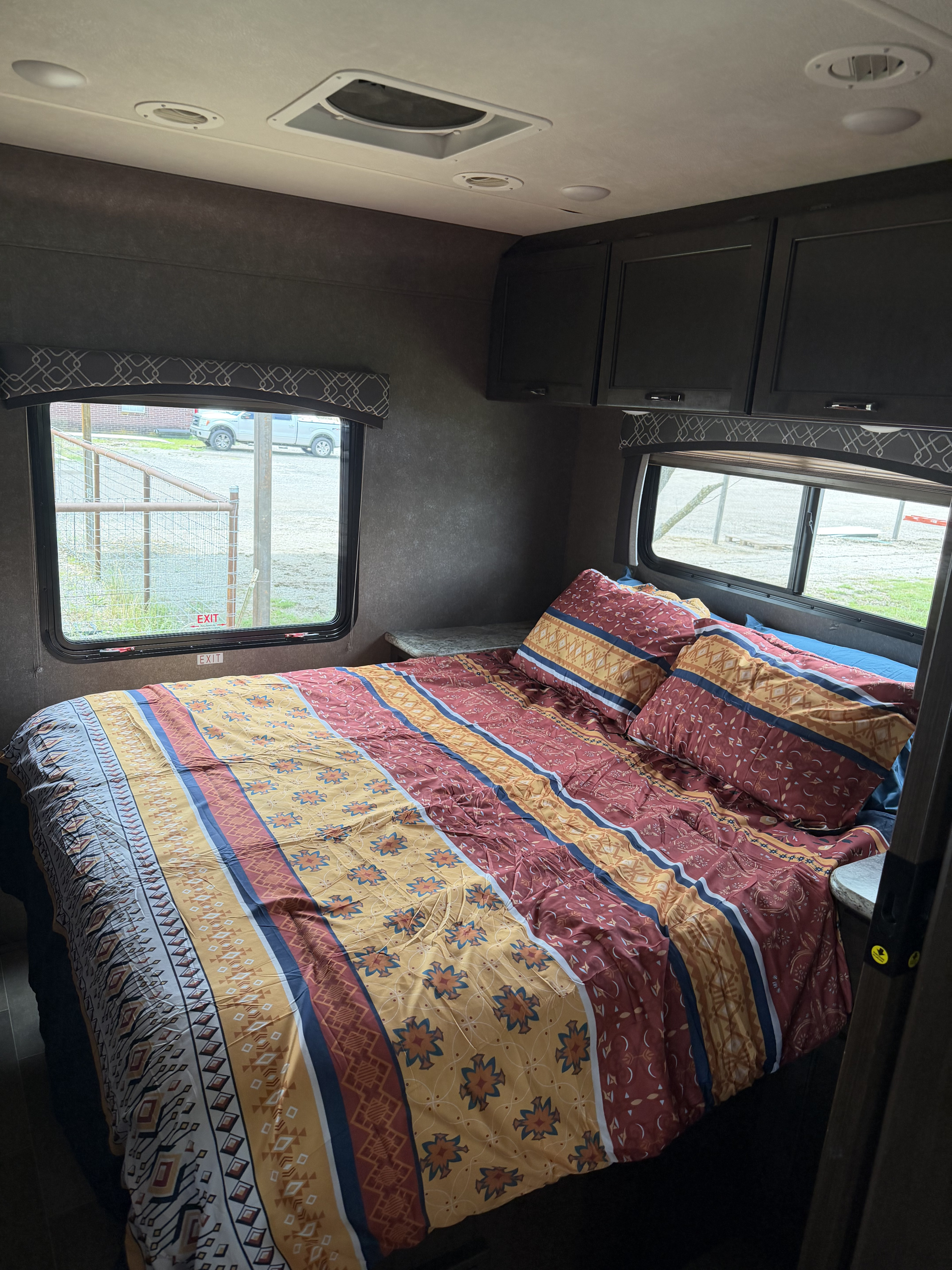 Discover this RV rental's cozy bedroom with vibrant patterned bedding, overhead storage, and windows showing the outdoor scene.. Thor Chateau 2020