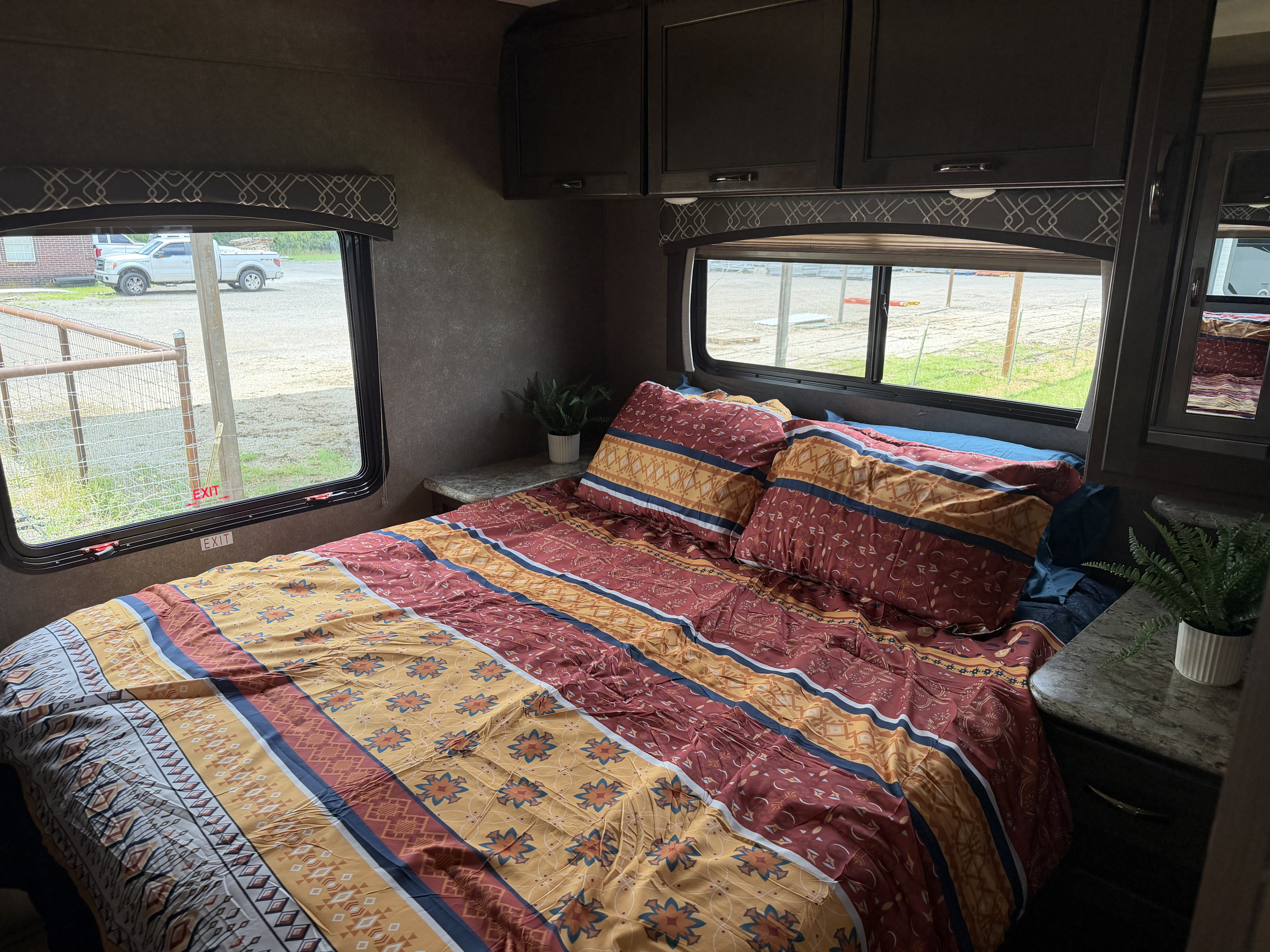 Cozy RV rental bedroom with colorful patterned bedding, overhead cabinets, and a window view. Ideal for your next road trip.. Thor Chateau 2020