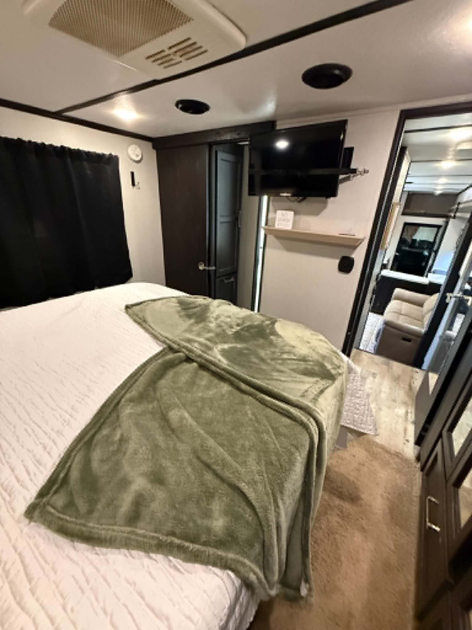 Comfortable RV rental bedroom featuring a bed with a green throw, TV, and blackout curtains. Relax on your road trip!. Keystone RV Fuzion Toy Hauler 2018