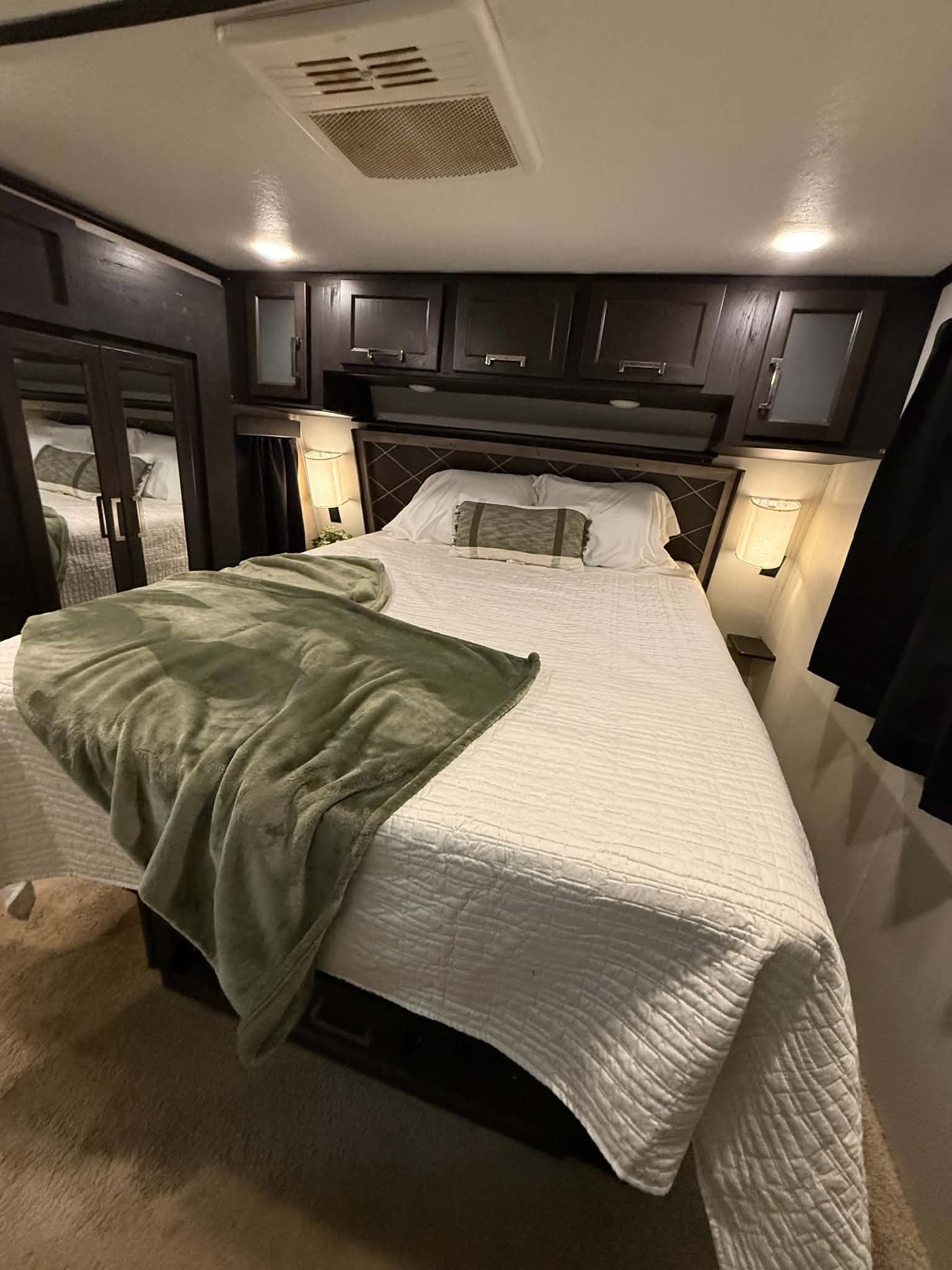 Inviting RV rental bedroom with a comfy bed, white and green bedding, overhead dark wood storage, and a ceiling AC unit.. Keystone RV Fuzion Toy Hauler 2018