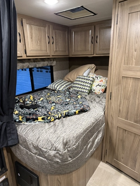 Cozy RV rental bedroom features a comfy bed, patterned pillows, storage cabinets, and a view from the window.. Coachmen Prism 2150 2018