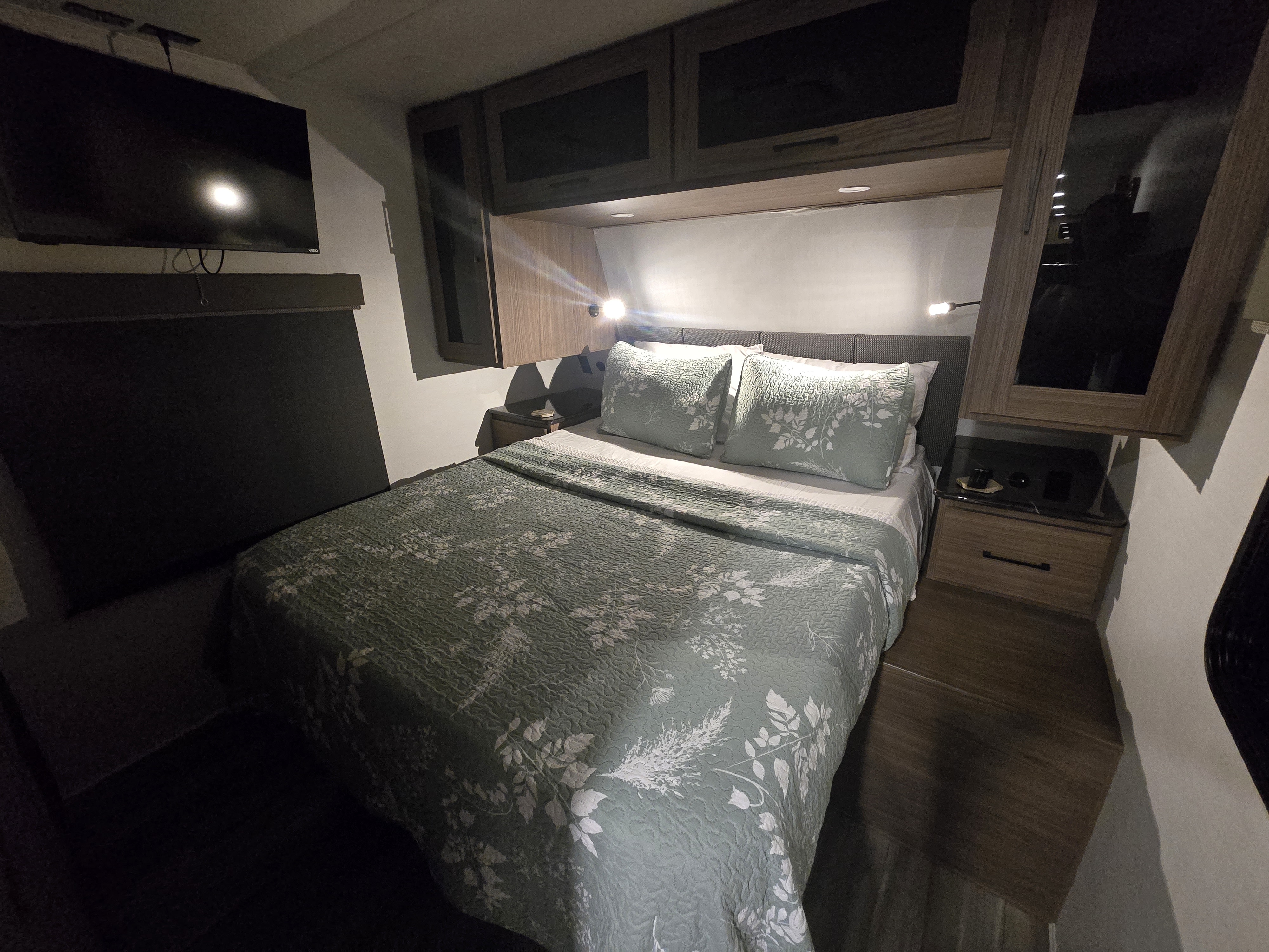Enjoy this comfortable RV rental bedroom, featuring a queen bed with patterned quilt, TV, and ample storage.. Alliance Delta 292RL 2025