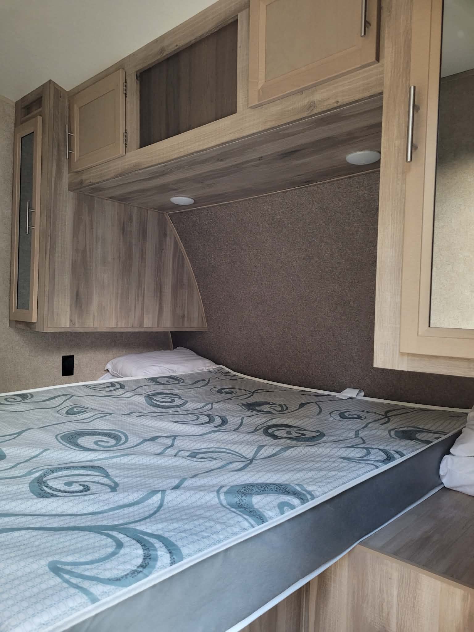 Comfortable RV rental bedroom with a patterned mattress, overhead cabinets, and built-in lighting for cozy stays.. Forest River Coachmen Catalina Legacy 2020