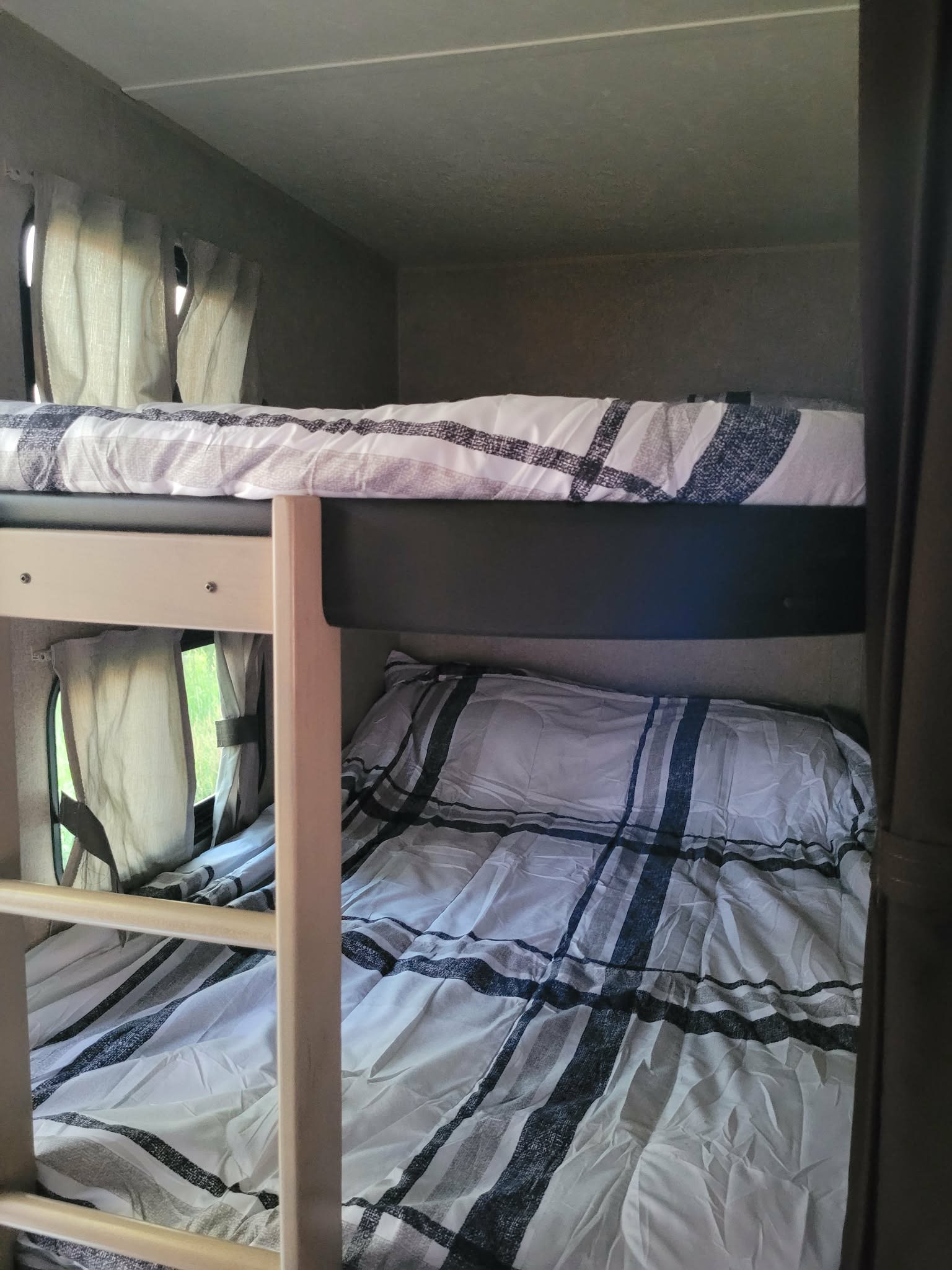 RV rental bunk beds offer cozy sleeping. Striped bedding, curtains & window view. Ideal for family travel accommodation.. Forest River Coachmen Catalina Legacy 2020