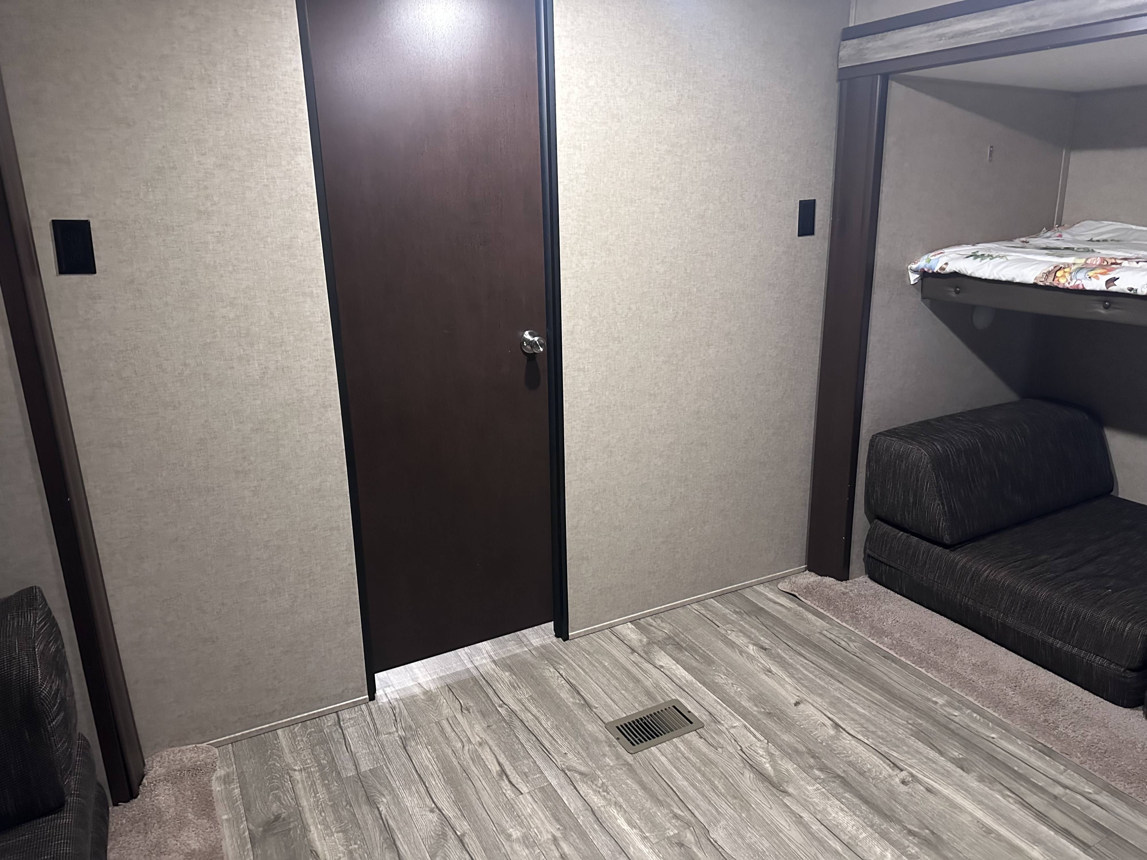 RV rental interior: a dark door, bunk bed with patterned comforter, textured walls, and wood-look flooring.. Forest River Cherokee 2017