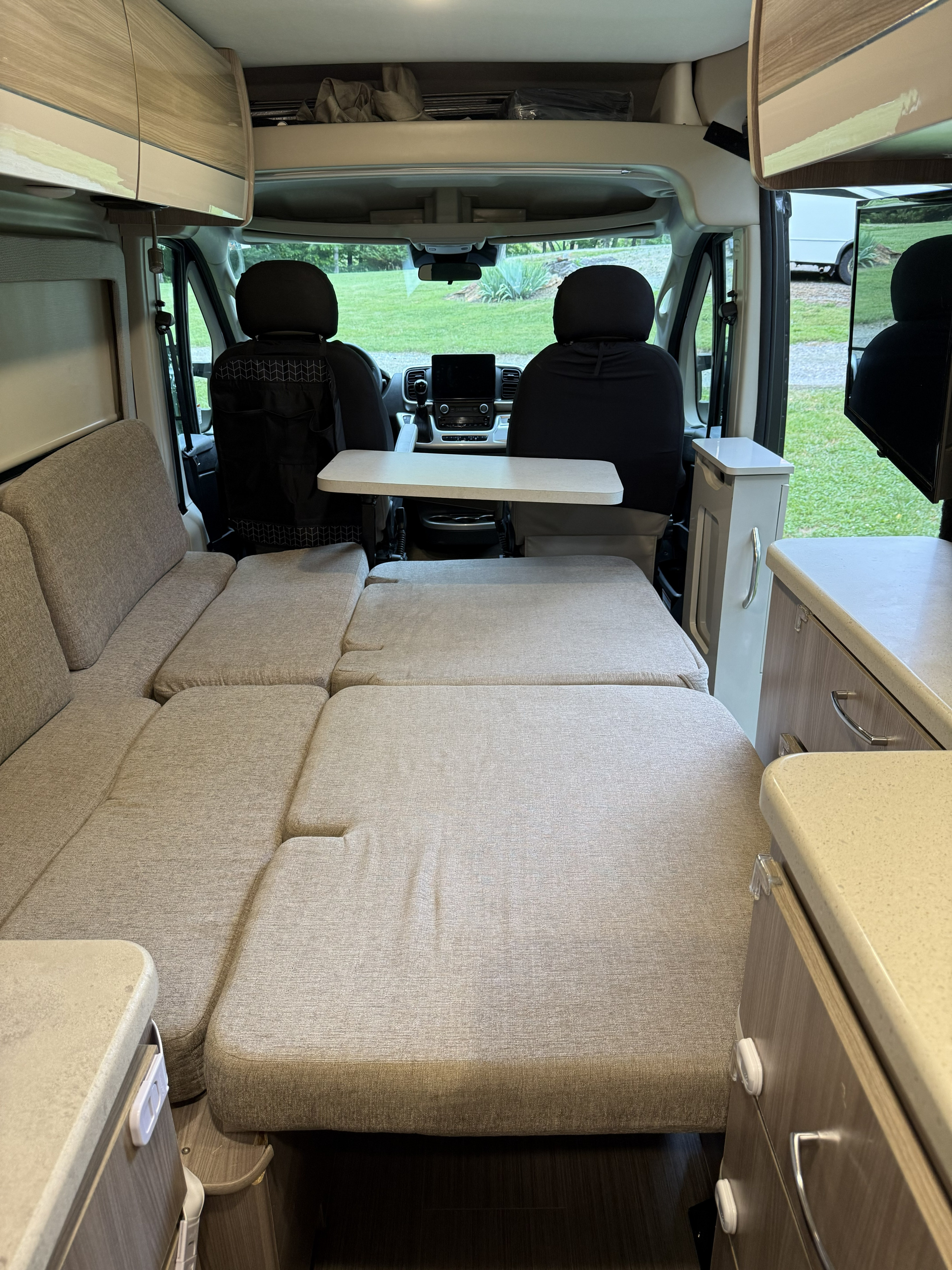 This rv rental showcases a versatile camper van interior, converting from seating to a comfortable bed setup, facing the cockpit.. Thor Sequence 2022