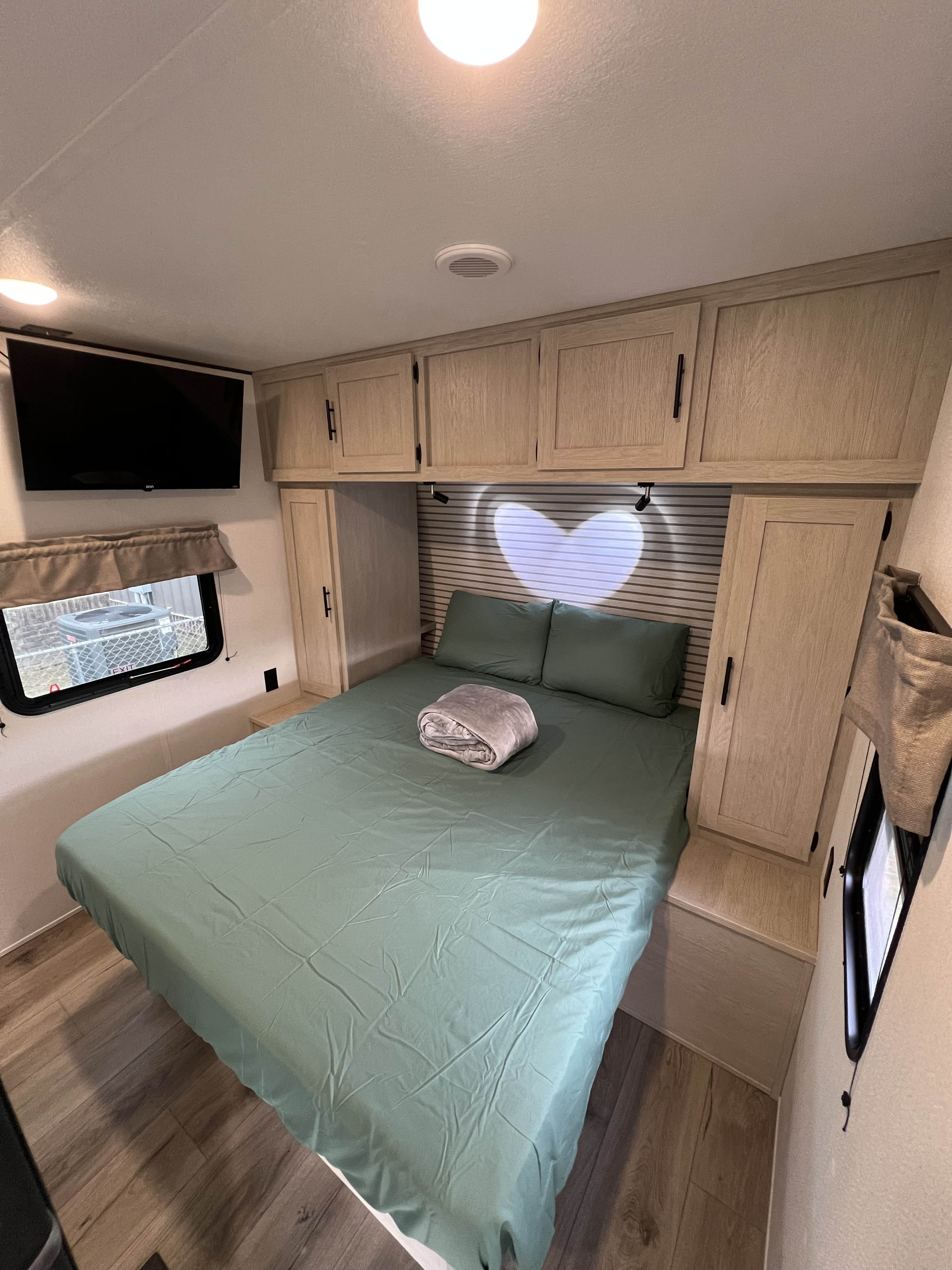 Cozy RV rental bedroom with a comfortable bed, storage, TV, and a unique heart-shaped light. Perfect for travel!. Forest River Shasta I-5 2026