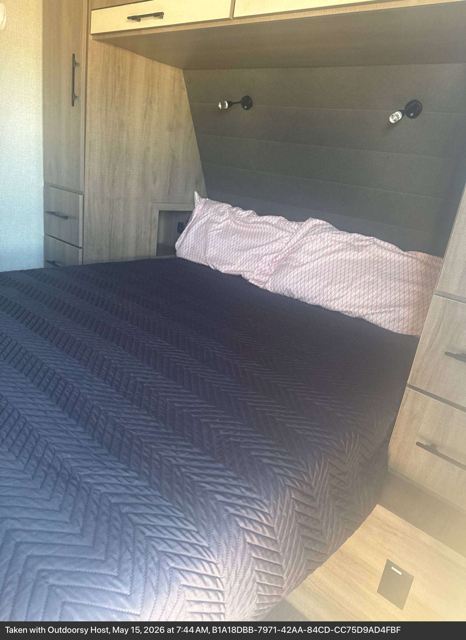 Comfortable RV rental bedroom featuring a bed with a dark blue chevron quilt, wood-grain cabinets, and reading lights.. Grand Design Imagine 2023