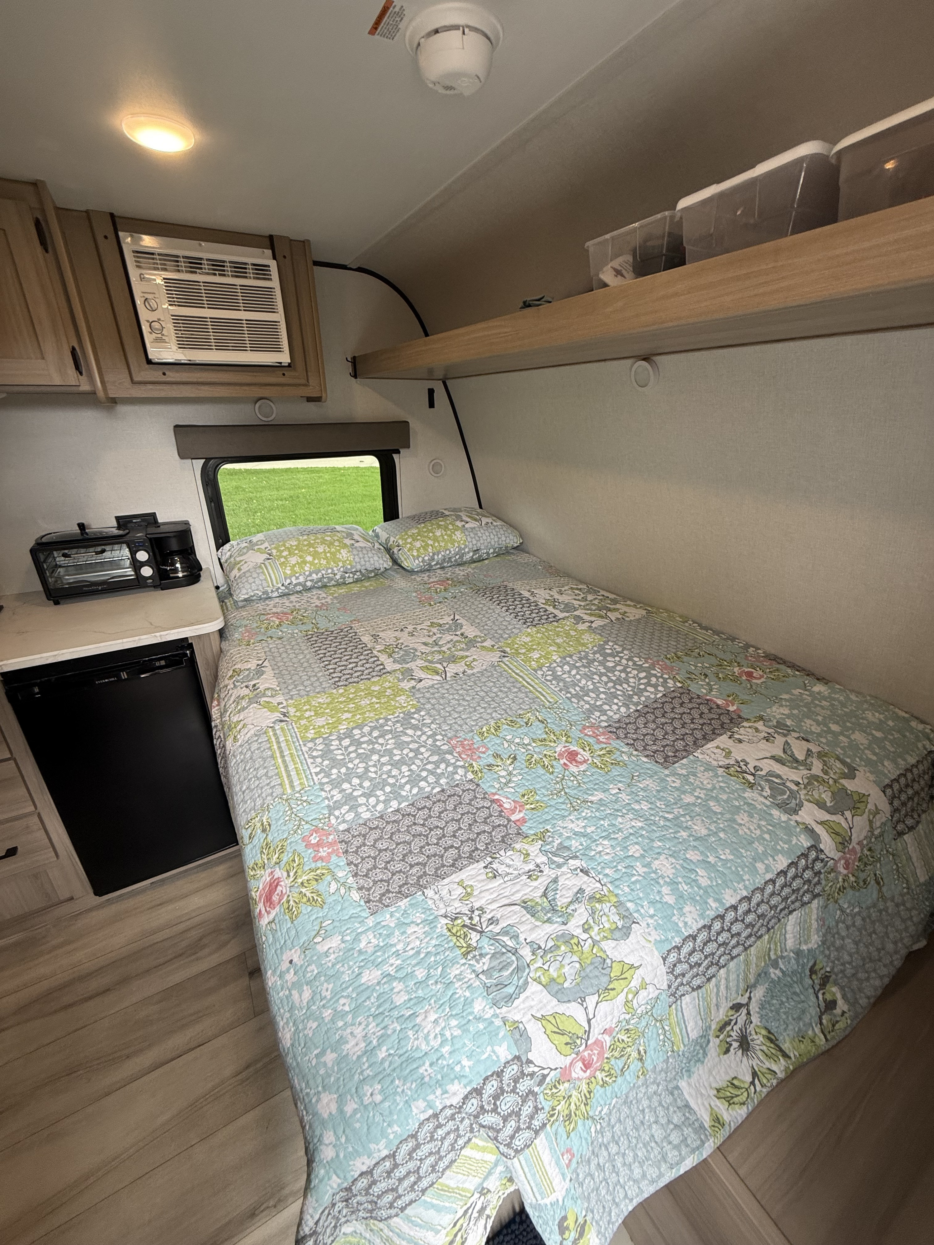 Cozy rv rental: a bedroom and kitchenette area with a colorful quilt, compact AC, mini-fridge, and toaster oven combo.. Keystone RV Coleman 13B 2026