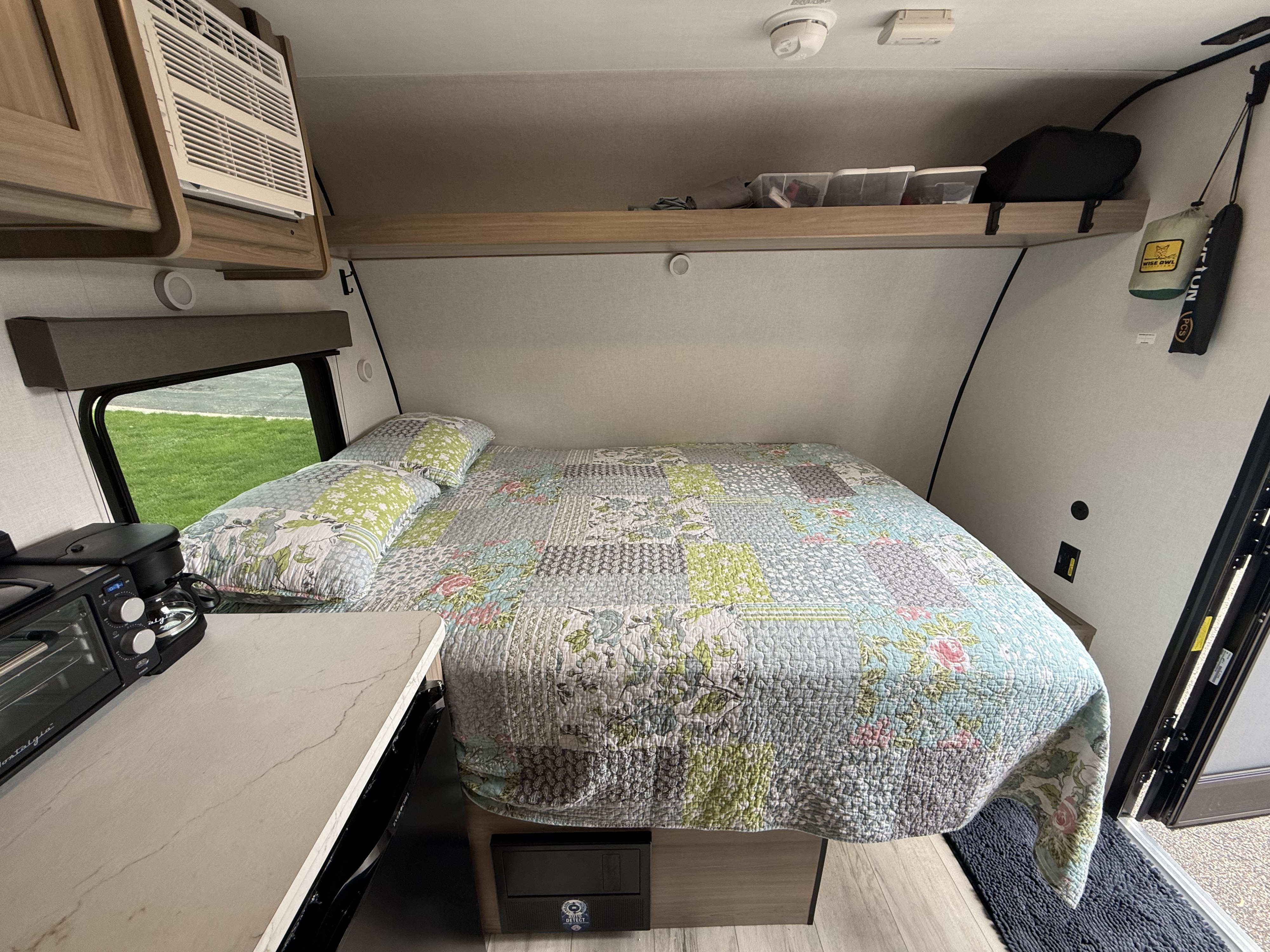 Cozy RV rental bedroom with a patchwork quilt, compact appliances, and an AC unit for comfortable travel.. Keystone RV Coleman 13B 2026