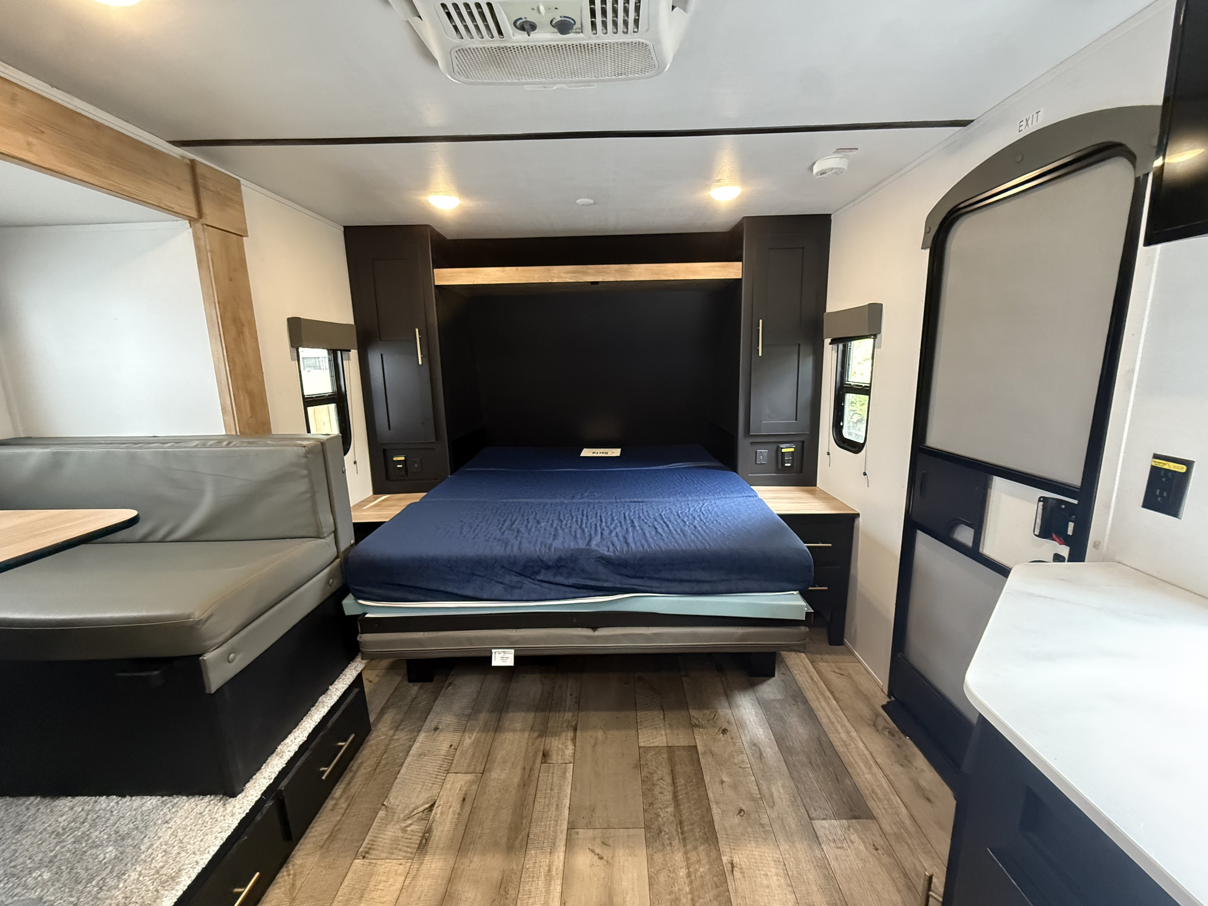 Modern RV rental interior featuring a blue murphy bed, gray dinette, dark cabinets, and wood-look floor.. Keystone RV Springdale 2022