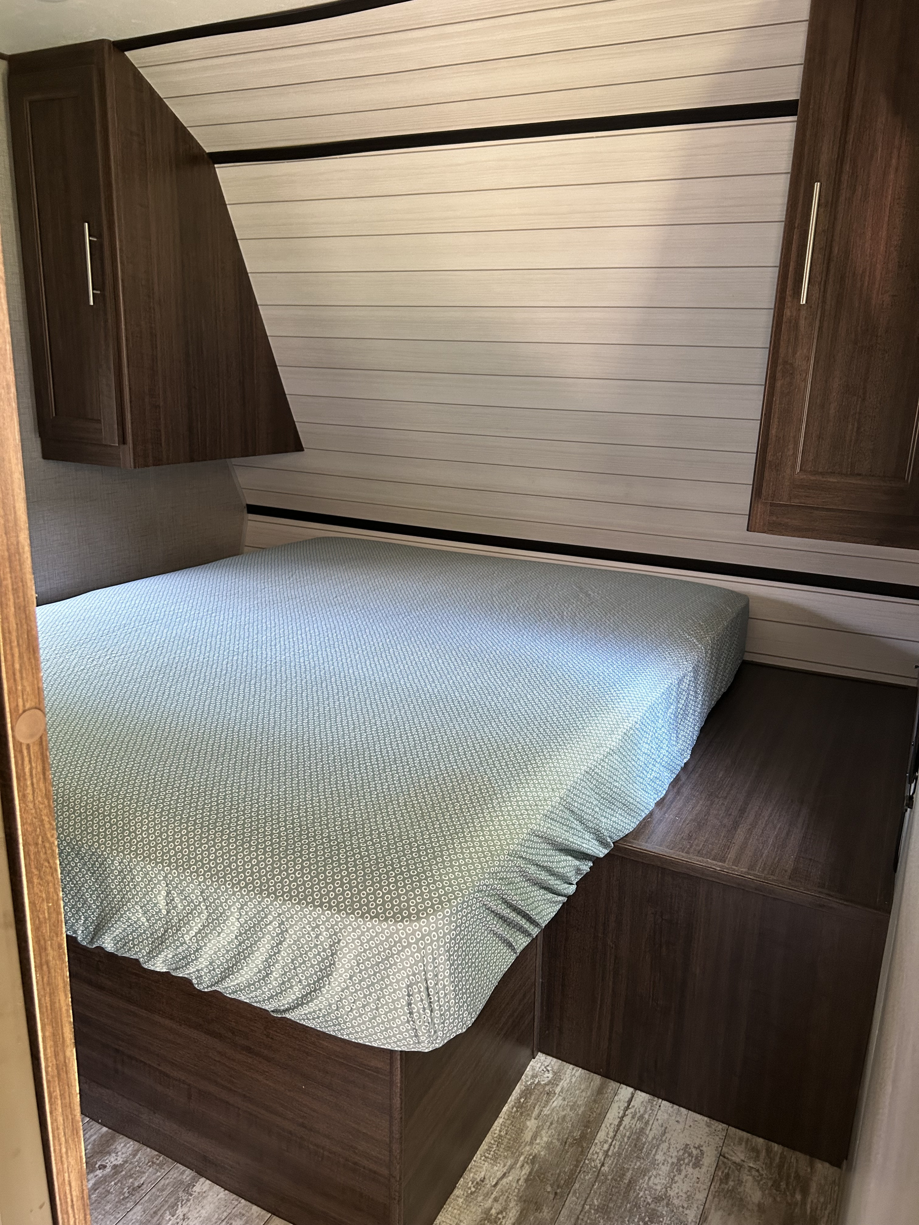 Compact RV rental bedroom featuring a patterned blue bed, dark wood cabinets, and light paneled walls.. Crossroads RV Zinger Lite 2019
