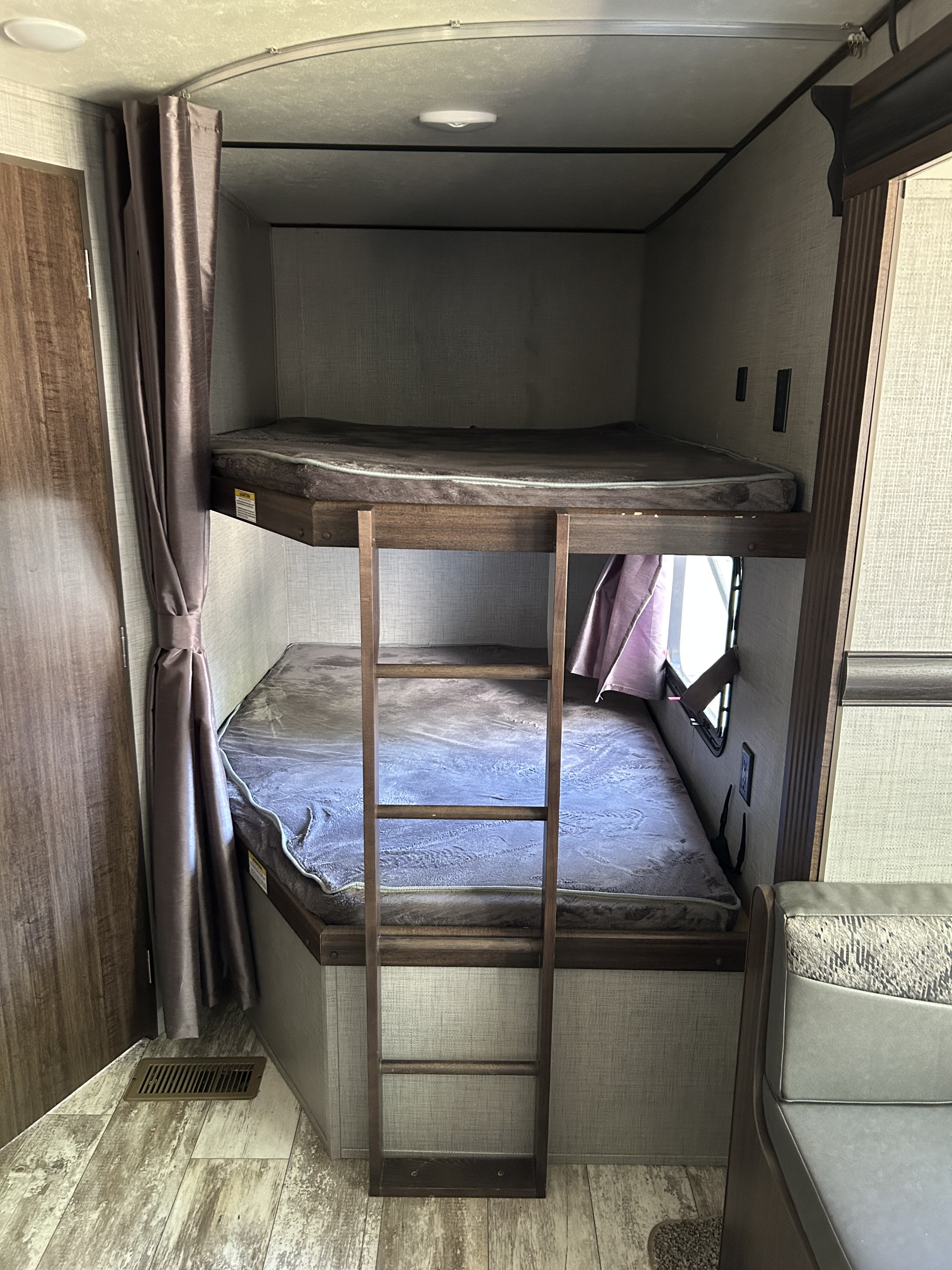 Interior of an RV rental showing bunk beds with ladder, mattresses, and privacy curtains, ideal for family travel.. Crossroads RV Zinger Lite 2019