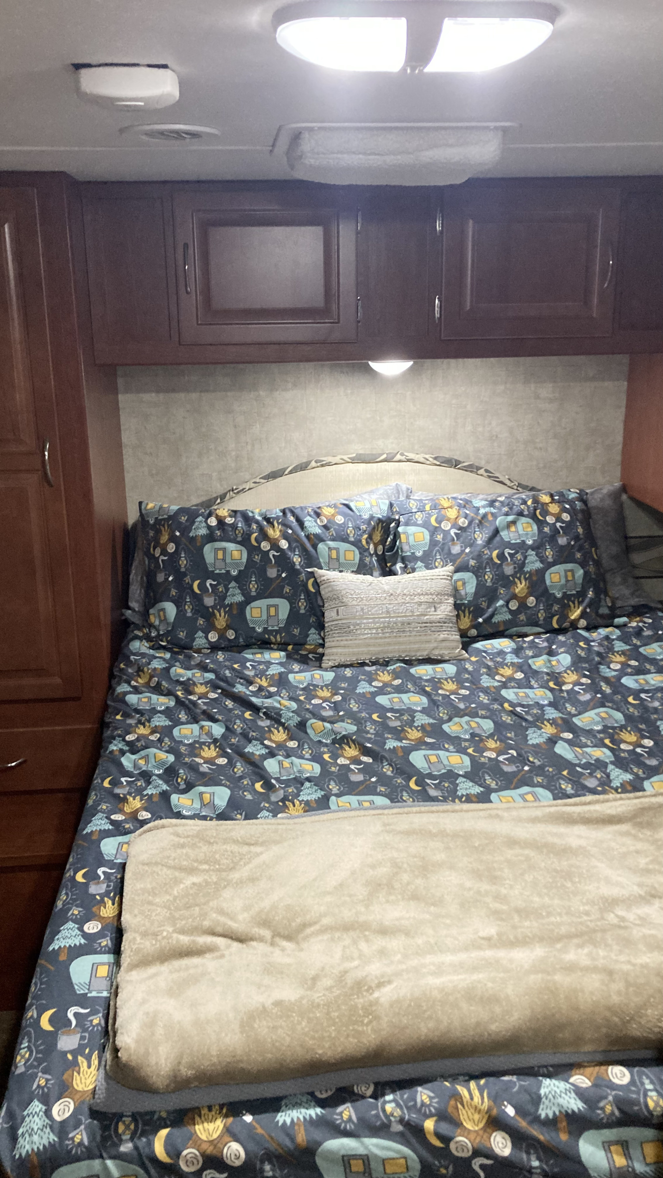 Cozy camper bedroom in an RV rental with camping-themed bedding featuring RVs, trees, and campfires, overhead cabinets, and a soft blanket.. Winnebago Minnie Winnie 2014