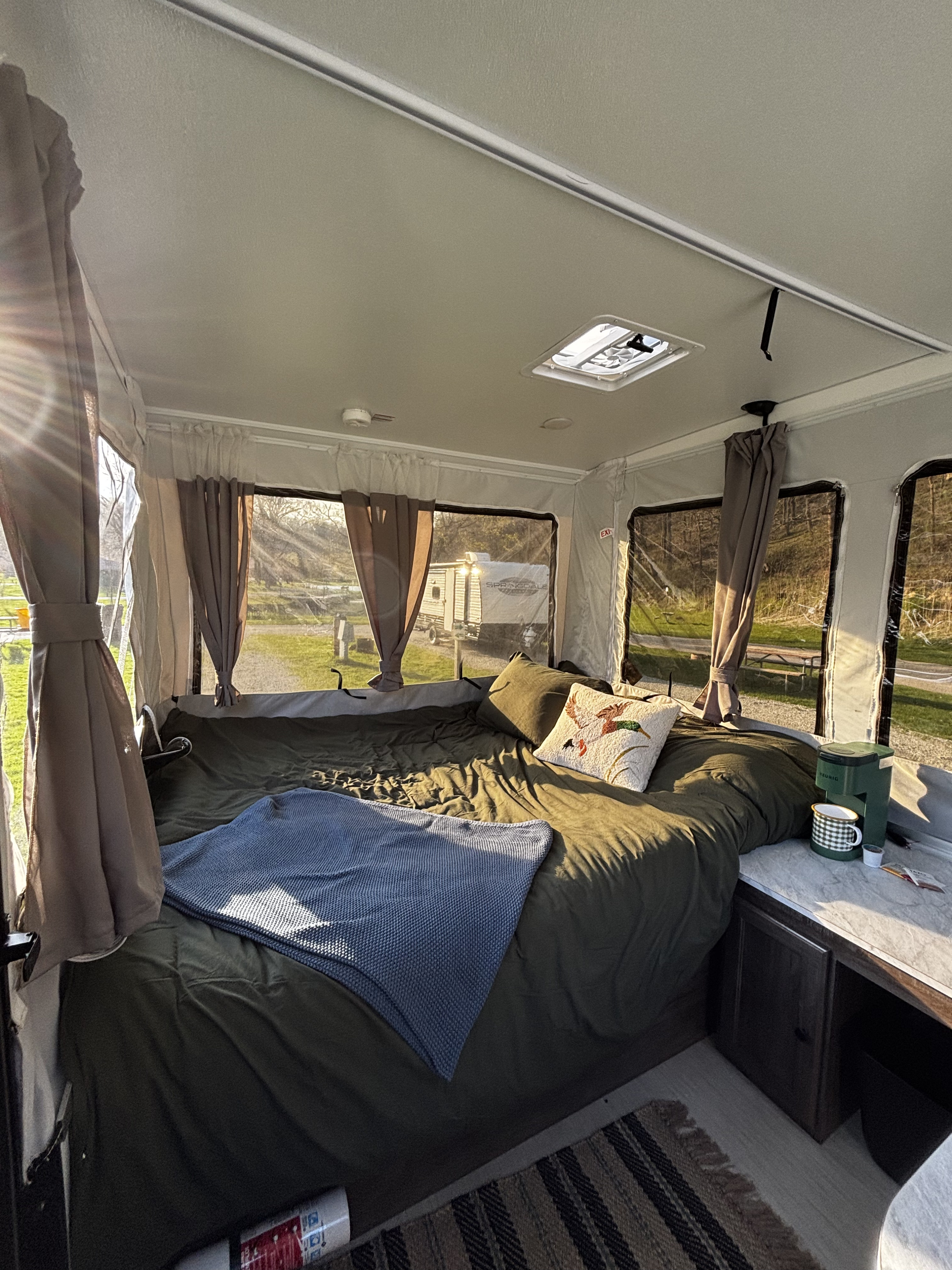 Cozy RV rental interior featuring a comfy bed, coffee maker, and sunlit views of a peaceful campsite.. Forest River Flagstaff OTG 2024
