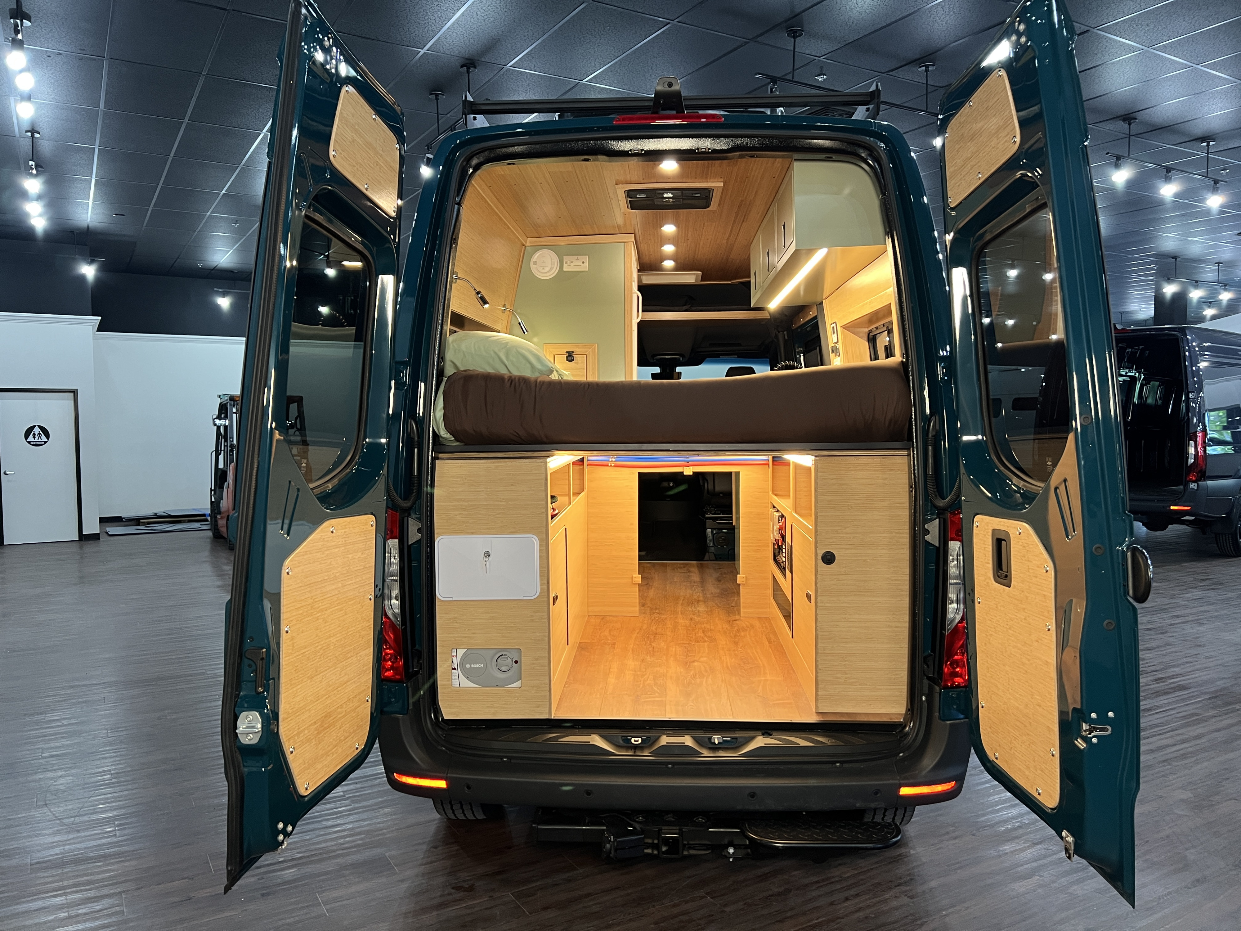 Inside a spacious RV rental camper van, revealing a meticulously designed interior with bed, wood accents, and bright lighting.. Mercedes-Benz Sprinter 2026