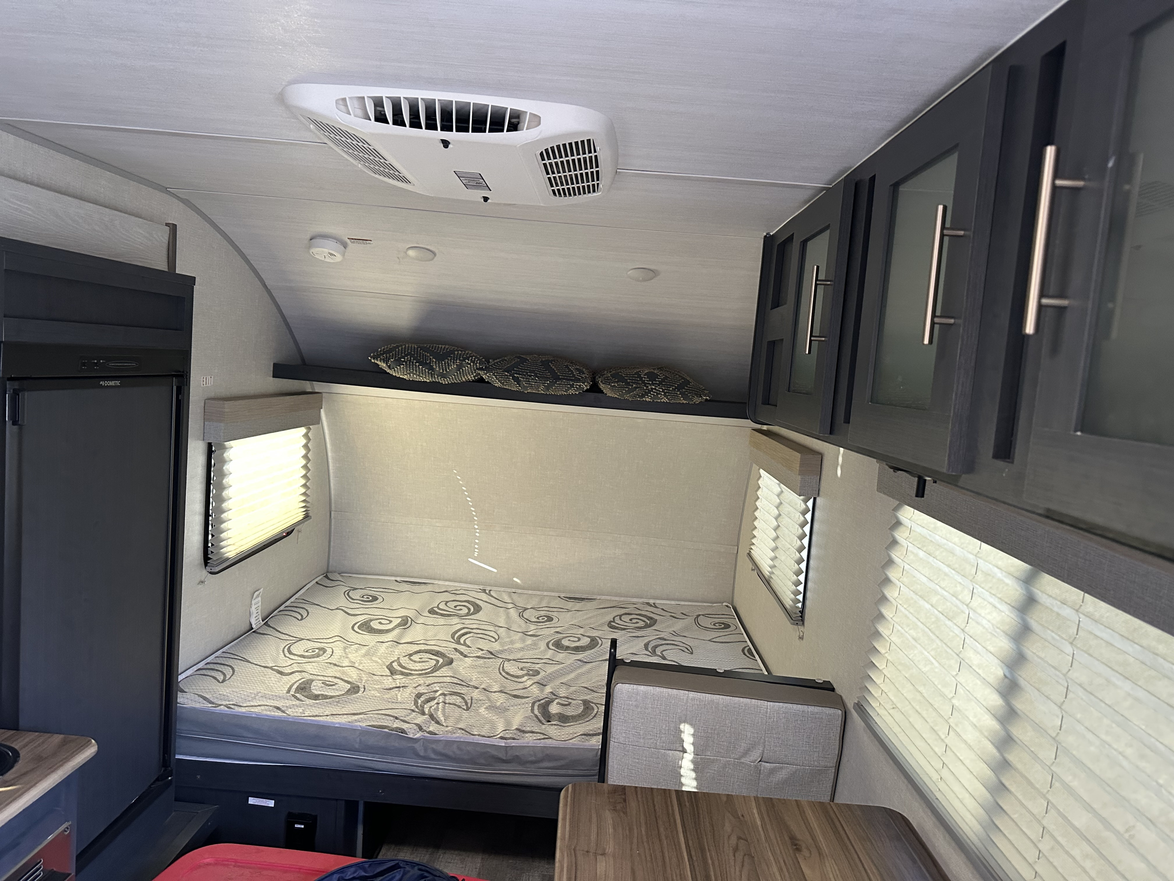 Inside an RV rental: a cozy bedroom area with a patterned mattress, window blinds, storage cabinets, and an AC unit.. Forest River R pod 2024