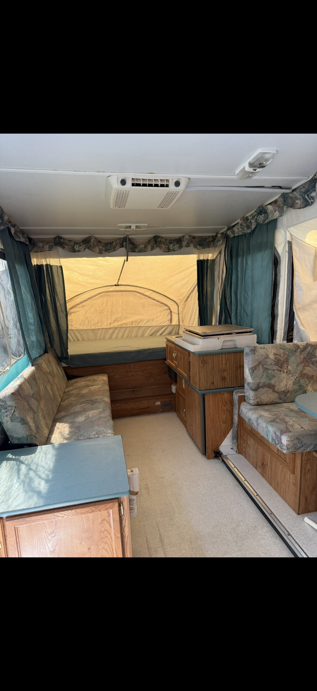 RV rental interior: A pop-up camper with bright bed area, patterned bench seating, wooden cabinets, and a ceiling AC unit.. Viking Pop Up 1999