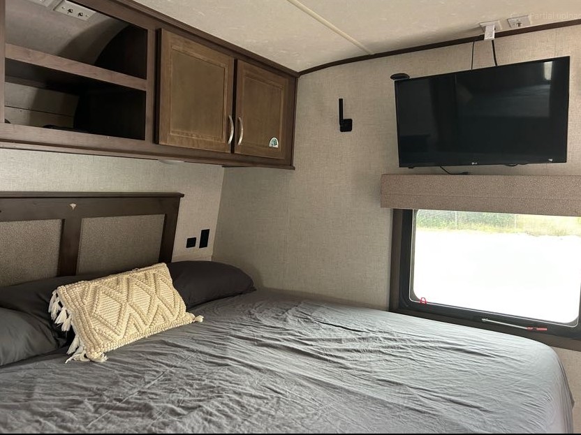 Spacious RV rental bedroom featuring a large bed, overhead storage, wall-mounted TV, and a window for comfortable trips.. Highland Ridge RV Open Range 2020