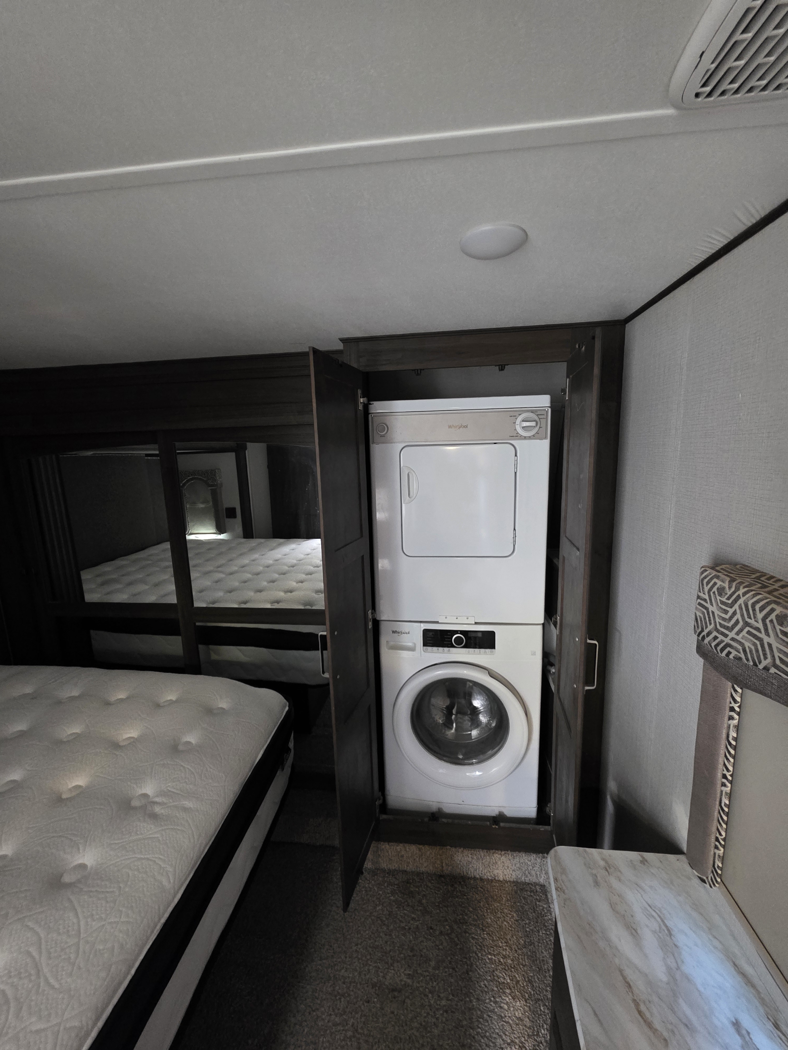 This rv rental bedroom provides a stacked Whirlpool washer and dryer within a wooden cabinet, offering laundry convenience.. Keystone RV Avalanche 2021