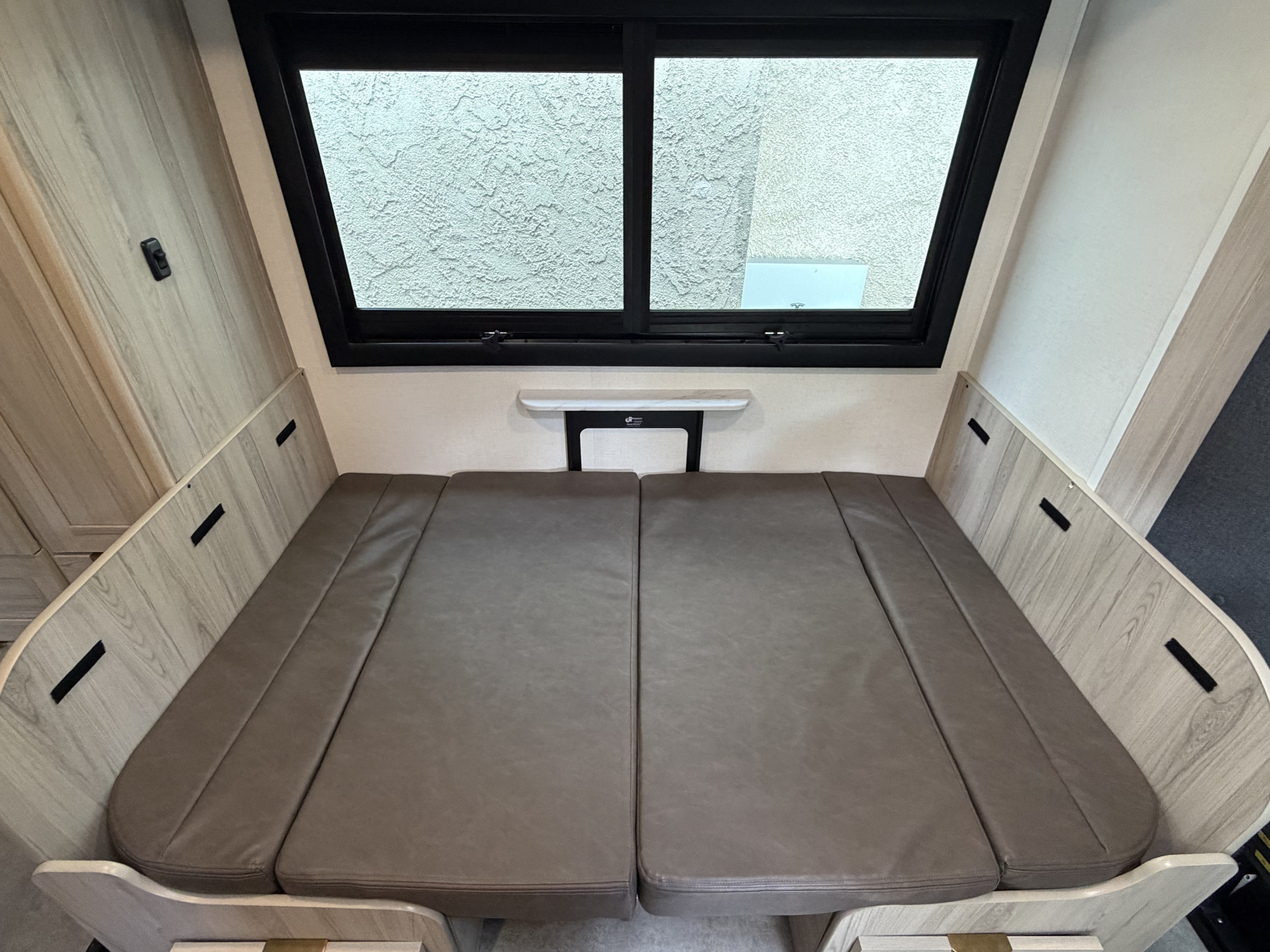 RV rental interior: a comfy grey cushion bed or dinette conversion. Light wood paneling & large window create a modern sleeping area.. Coachmen Prism 2026