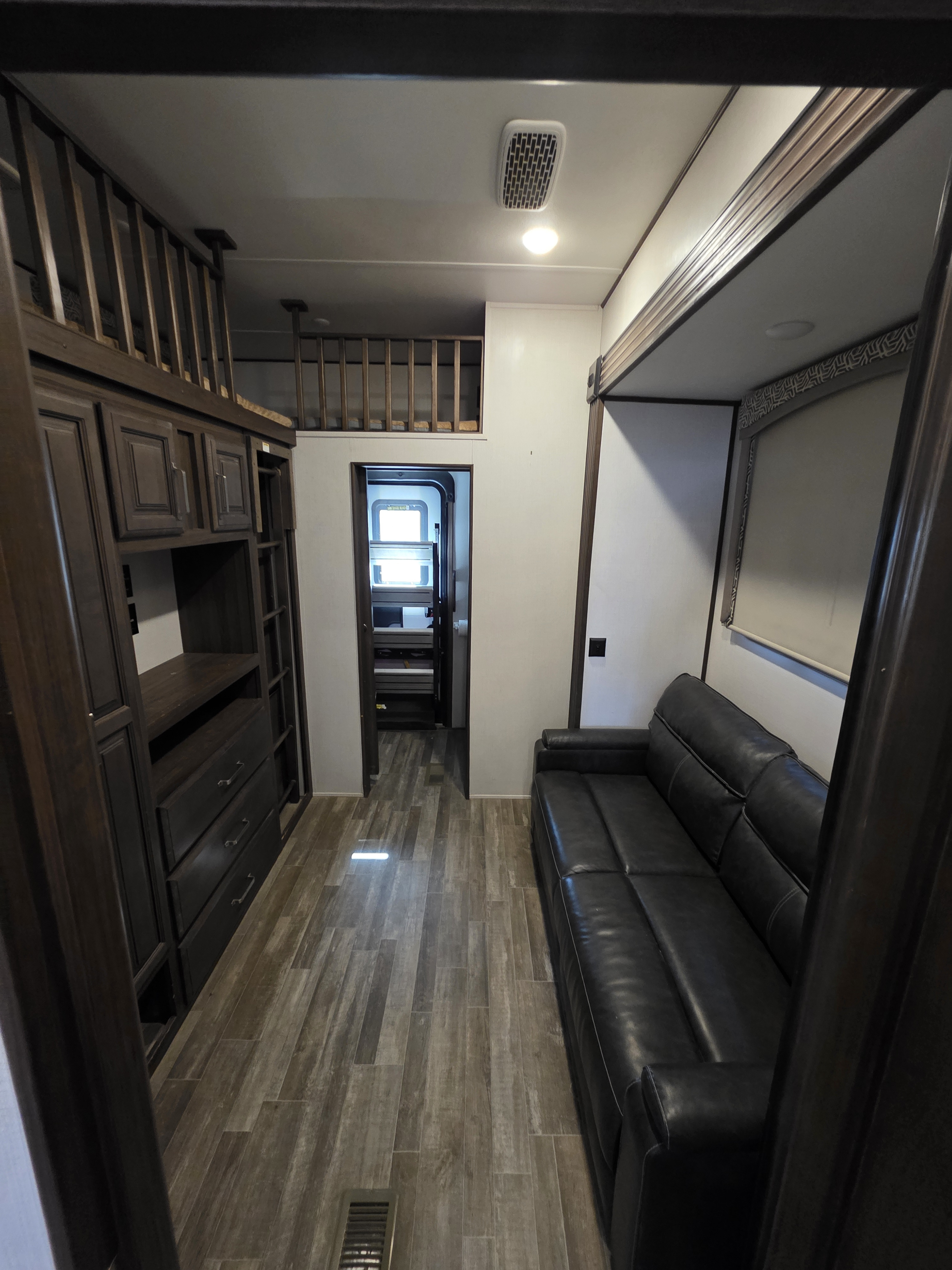 Modern RV rental interior with a dark leather sofa, built-in cabinetry, wood flooring, and two visible loft areas.. Keystone RV Avalanche 2021