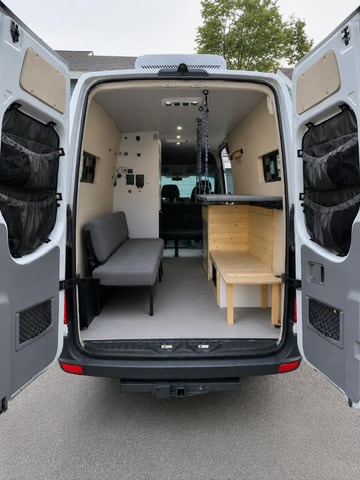 RV rental camper van interior. Rear doors open to reveal bench seating, storage, and a suspended bed, ready for adventure.. Mercedes-Benz Sprinter 2016