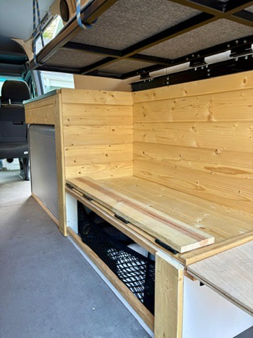 RV rental van conversion: custom wooden bench, backrest, under-seat storage net, and an overhead bed platform.. Mercedes-Benz Sprinter 2016