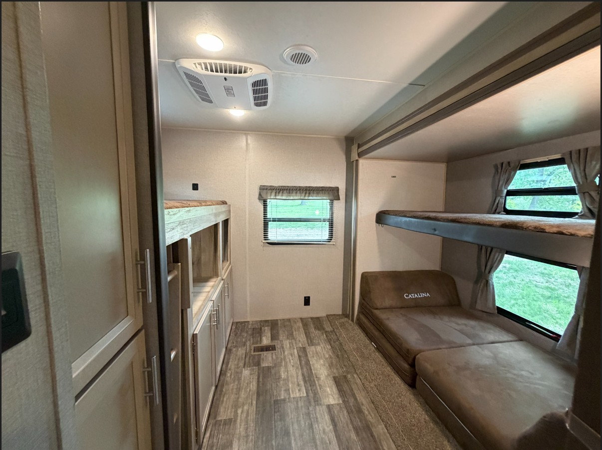 Inside an RV rental bunkhouse: two bunk beds, a convertible sofa, storage cabinets, and windows.. Coachmen Catalina Legacy 2022