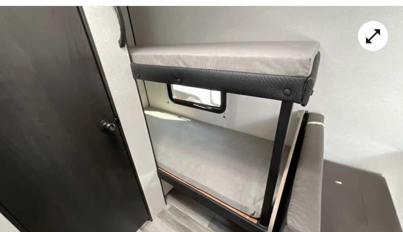 Interior of an rv rental: cozy bunk beds with light mattresses, an upper window, and a dark door.. Jayco Jayco 2026