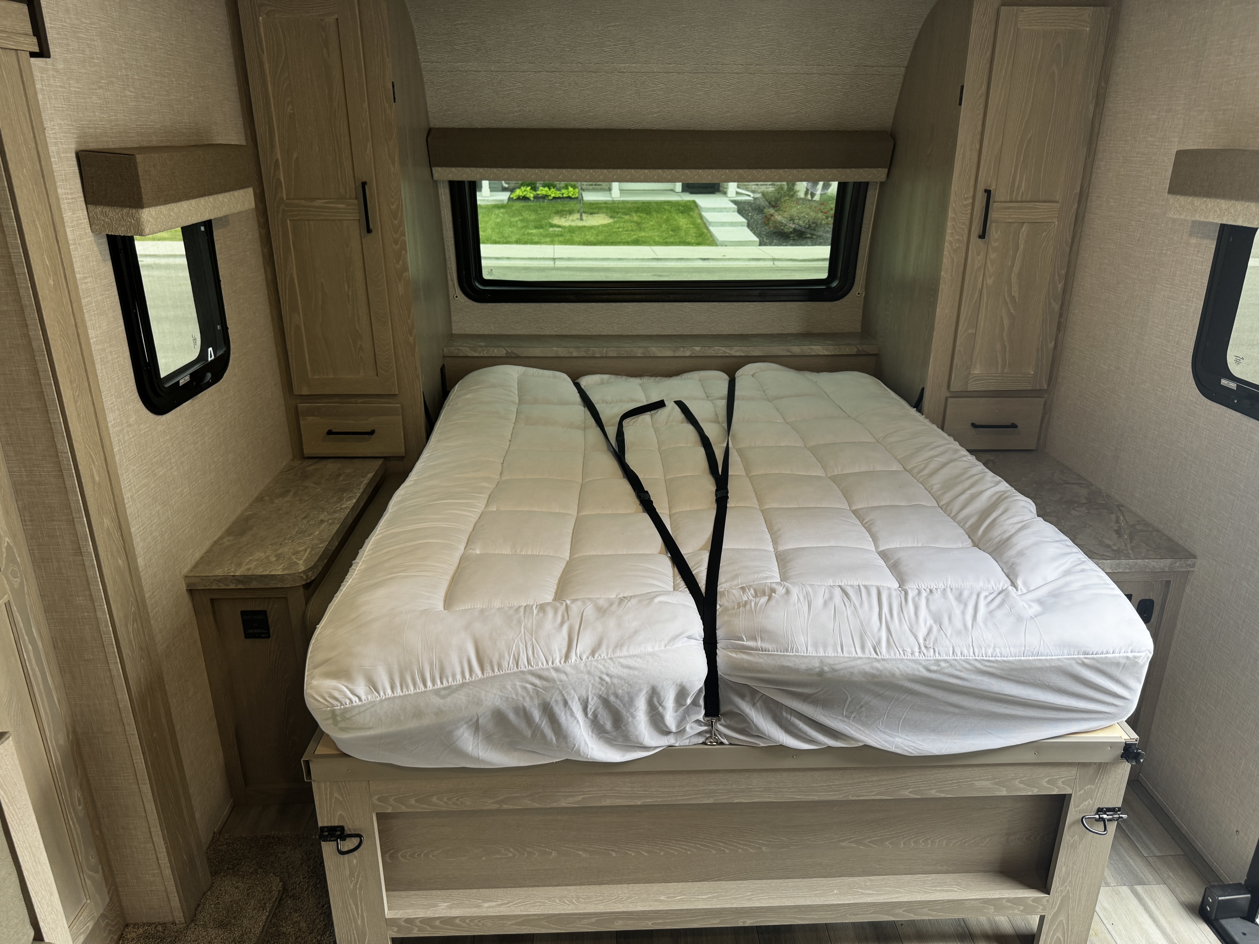 RV rental bedroom showing a split mattress, wood cabinetry, and windows overlooking a neighborhood.. Forest River Flagstaff Micro Lite 2022