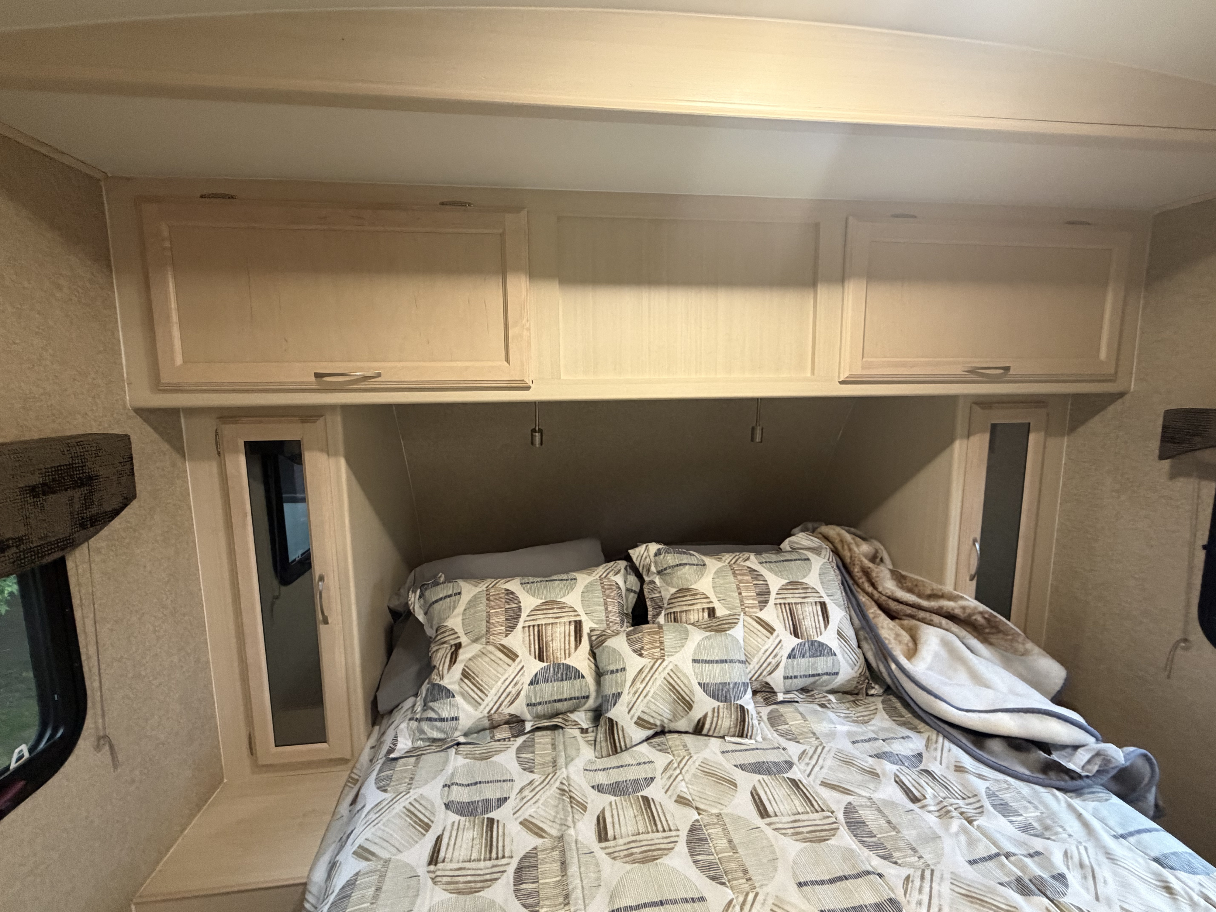Cozy RV rental bedroom featuring patterned bedding, overhead cabinets, and integrated reading lights.. Minnie Minnie Plus 2019