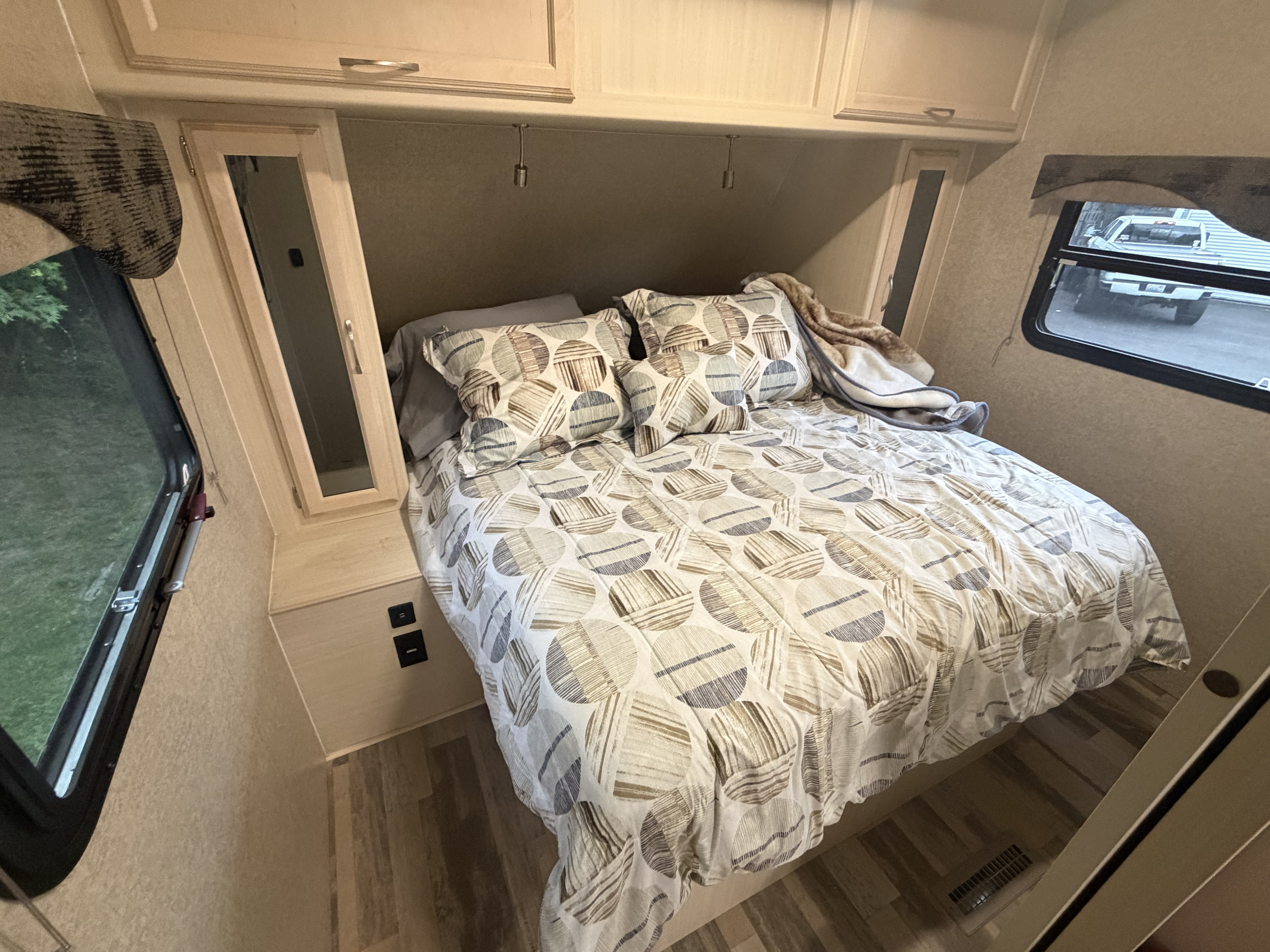 Cozy RV rental bedroom features a patterned bed, overhead storage, side cabinets, and windows, ideal for compact travel.. Minnie Minnie Plus 2019