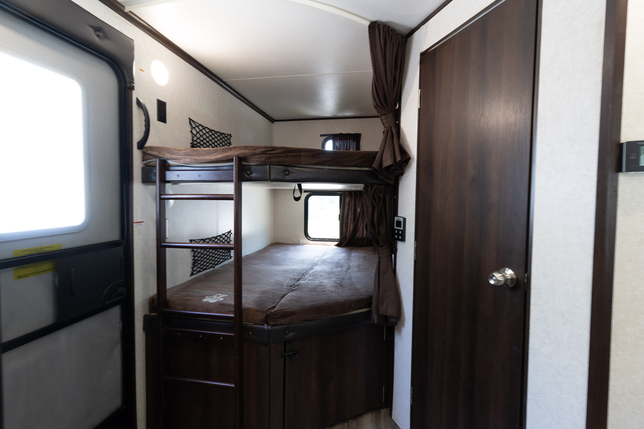 Inside an RV rental: dark wood bunk beds with ladder, windows, & door, ideal for road trips.. Jayco Jay Flight 2019