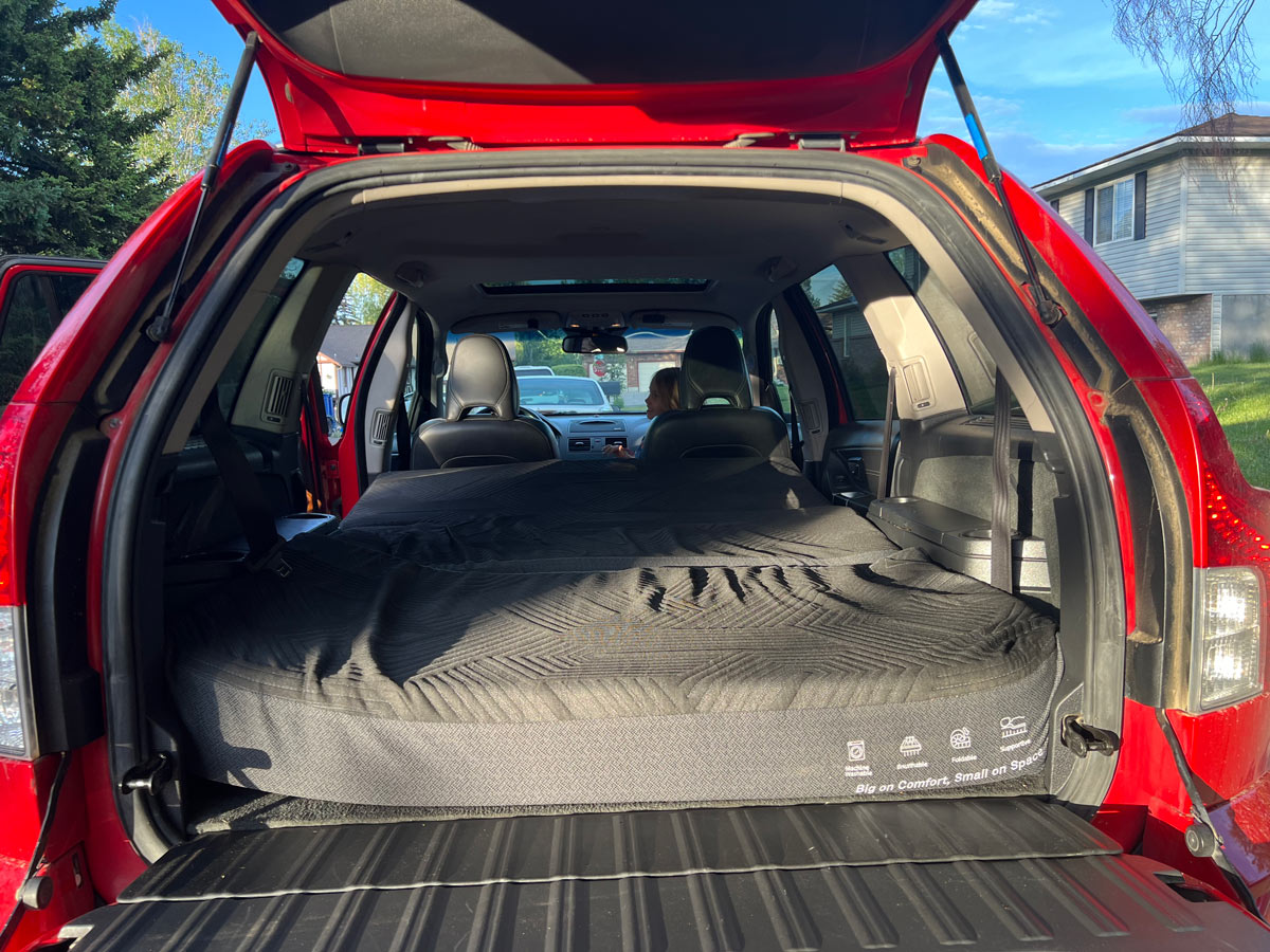 Red SUV with tailgate open, showing a black foldable mattress for car camping. A comfortable alternative to an RV rental.. Volvo xc90 2014